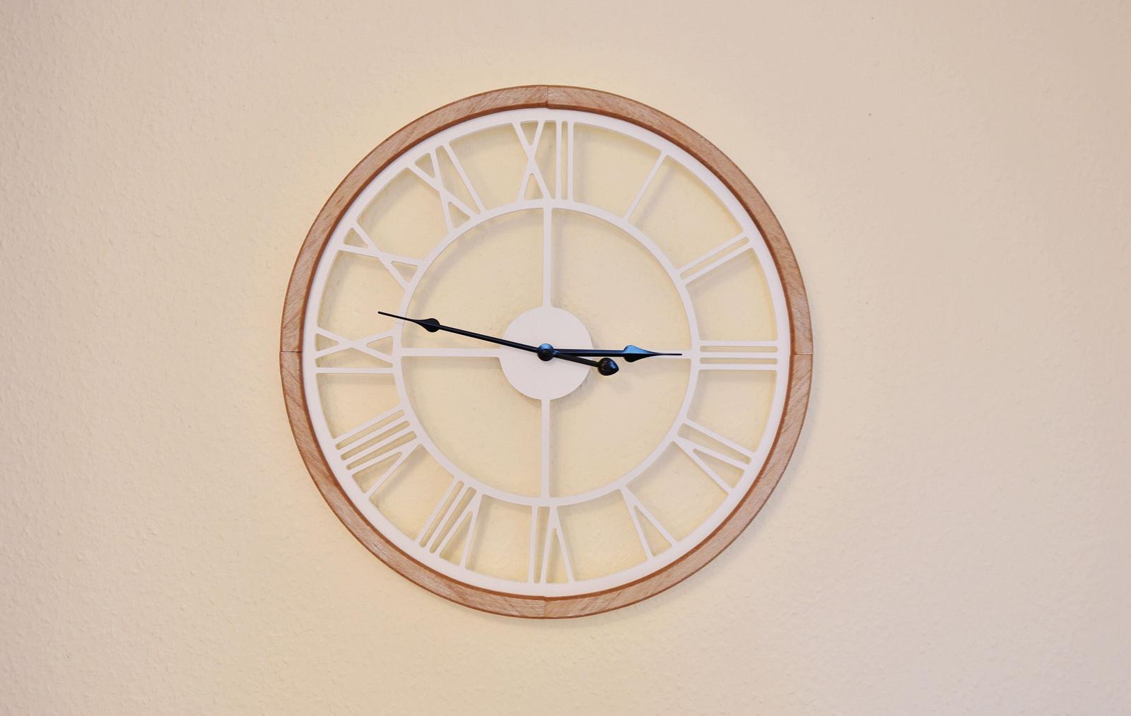 A wall clock with a wooden frame and Roman numerals on the wall.