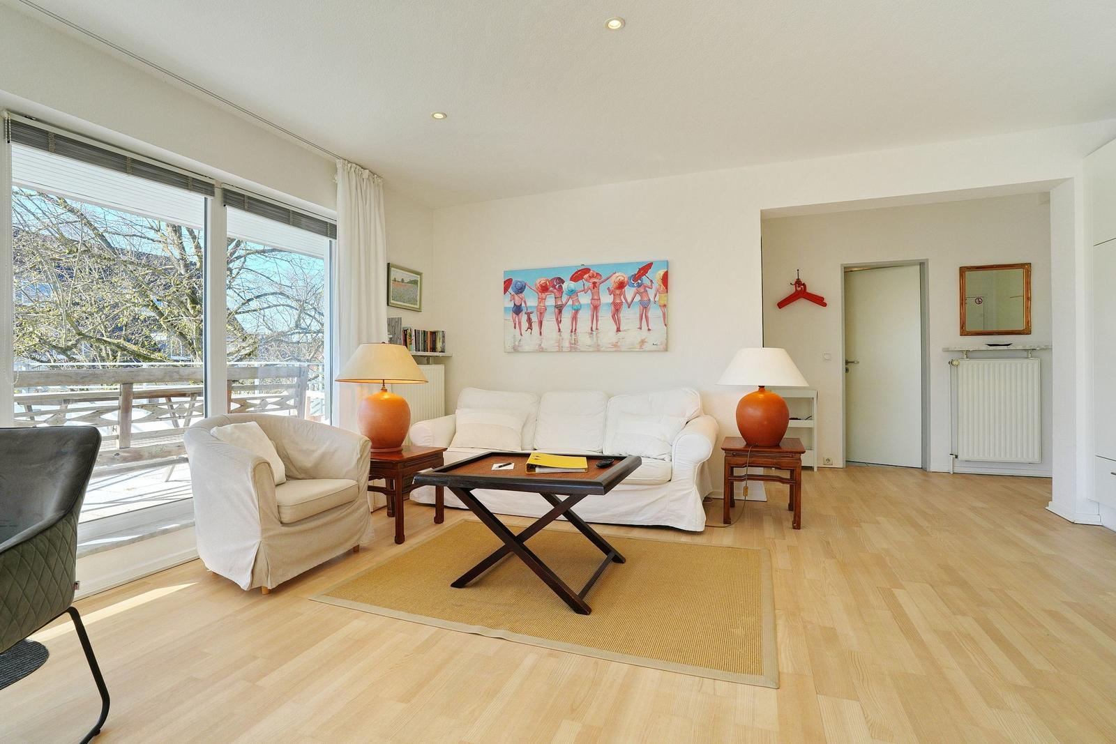 Wohnzimmer mit Sofa, Sessel und Tisch. Große Fenster, Wandbild und Holzboden.