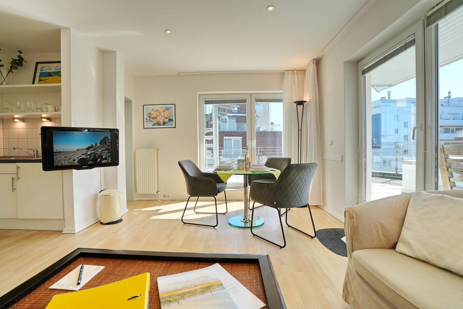 Wohnung mit Essbereich, Sofa und TV. Terrasse mit Blick auf Gebäude.