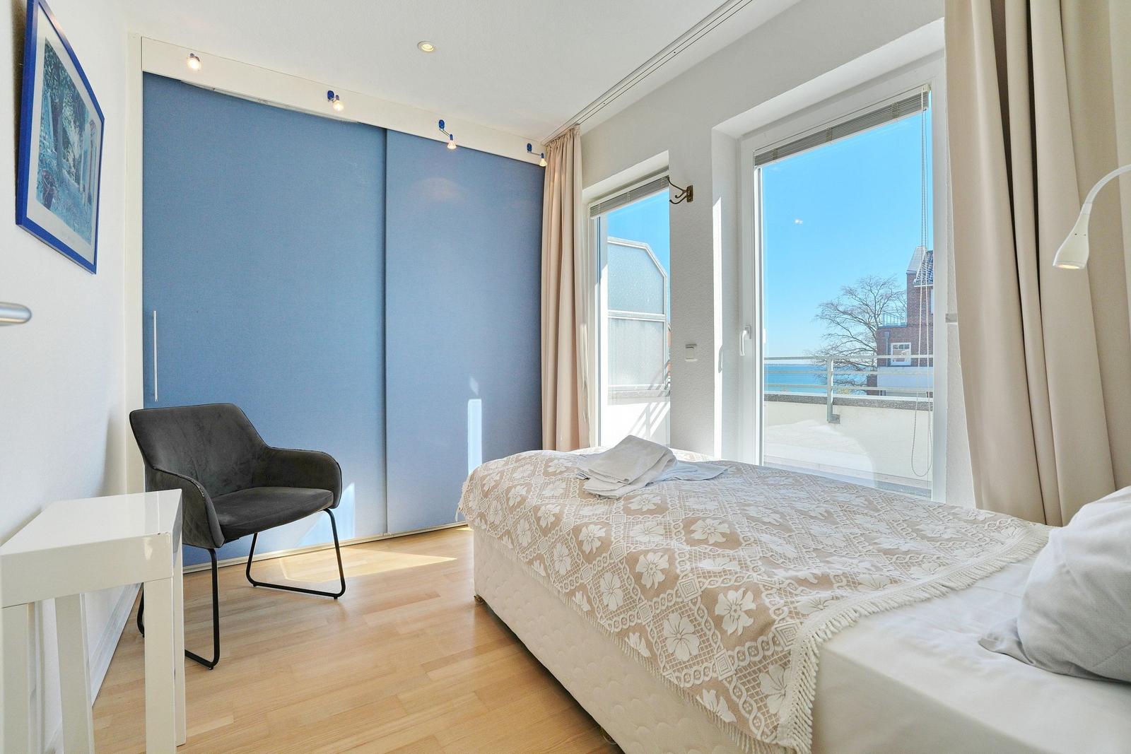 Schlafzimmer mit Bett, Stuhl und Blick auf Balkon.