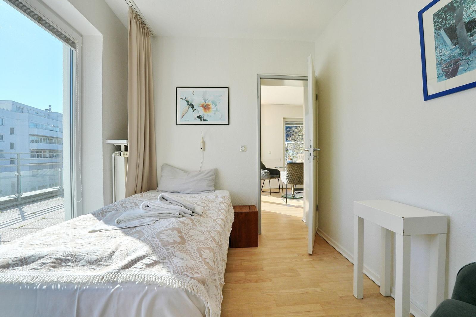 Schlafzimmer mit Bett, Fenster und Tisch. Durchgang zur Küche.
