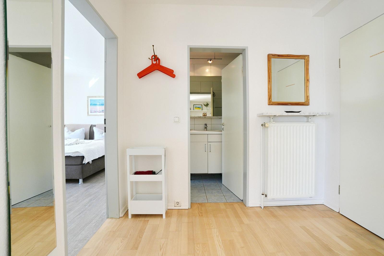 Flur mit Holzboden, Spiegel, Heizung und Blick in Schlafzimmer und Bad.