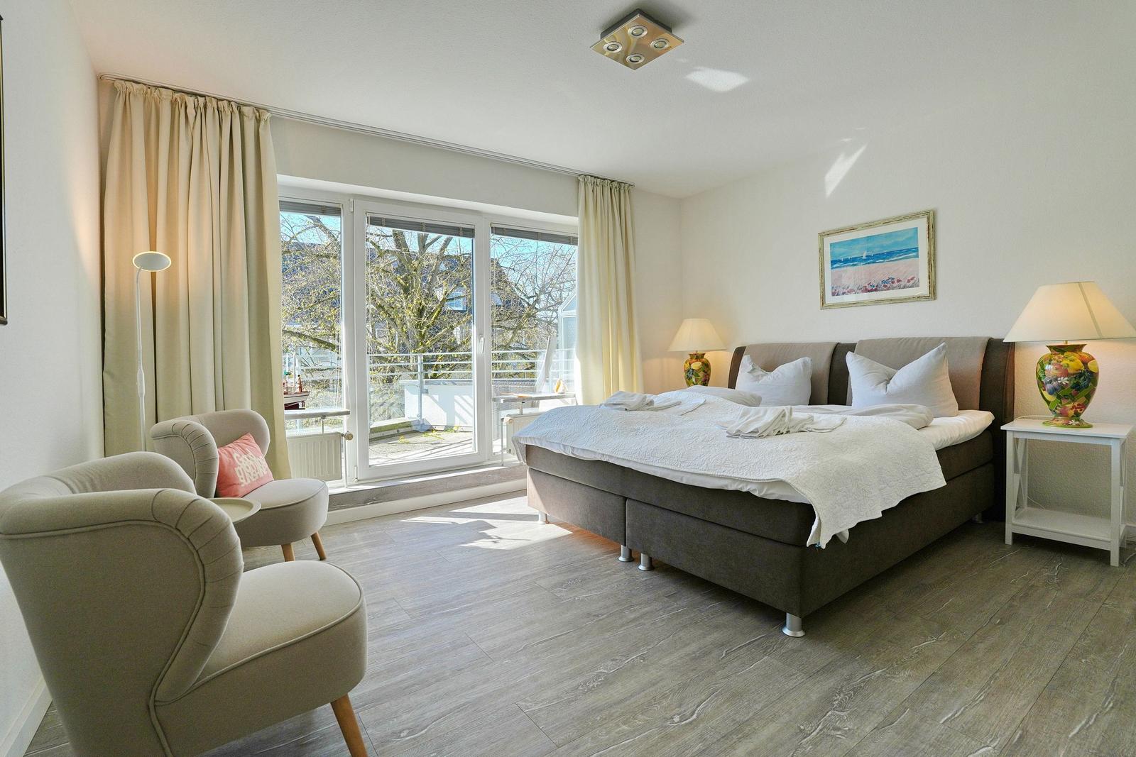Schlafzimmer mit Bett, zwei Sesseln und Balkonzugang.
