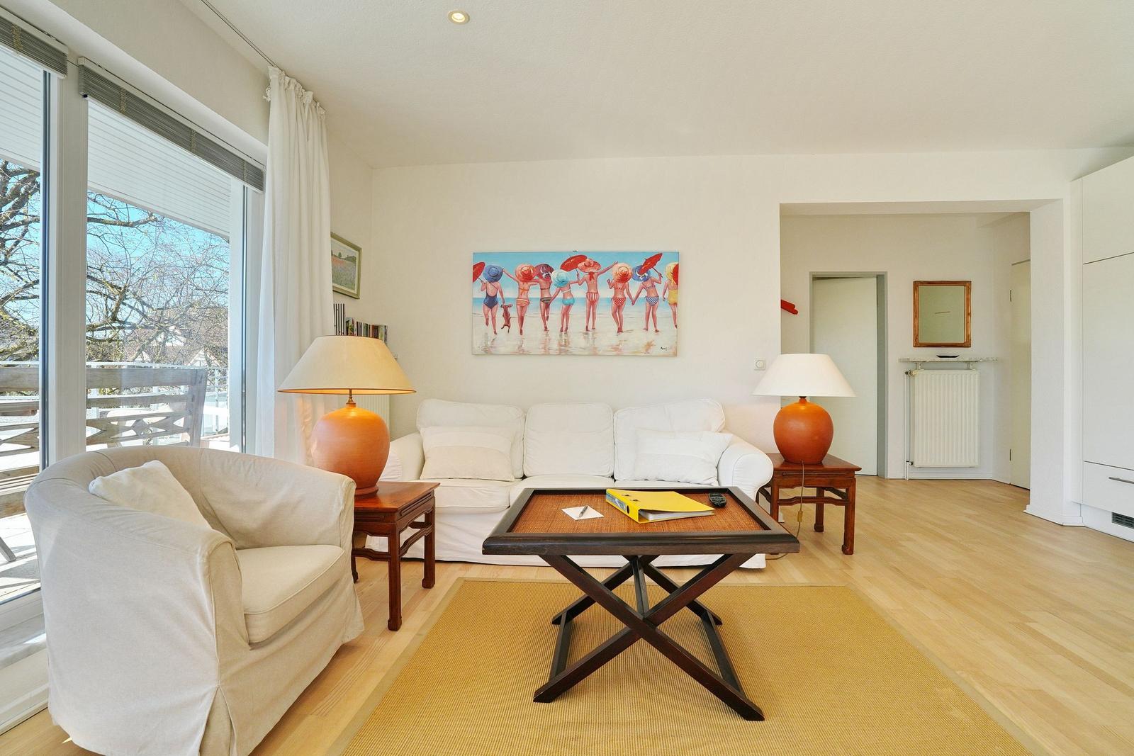 Wohnzimmer mit weißem Sofa, Holztisch und Fenster zum Balkon.