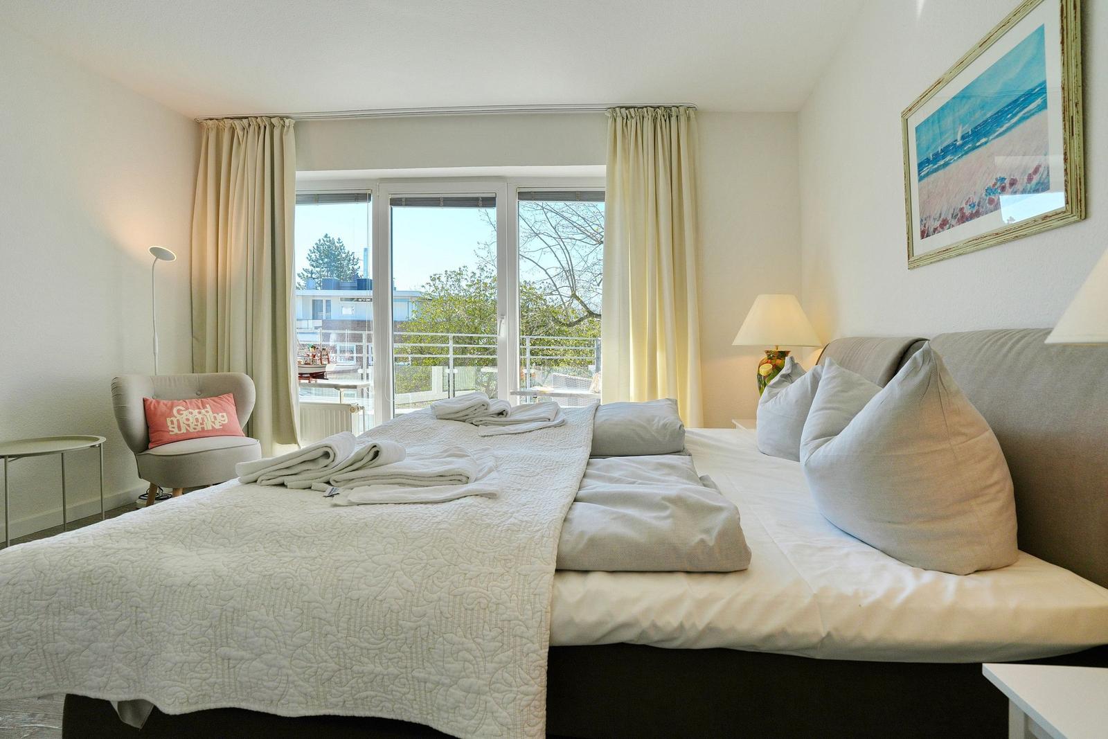 Schlafzimmer mit großem Bett, Fenster und Balkon. Wandbild und Nachttische.