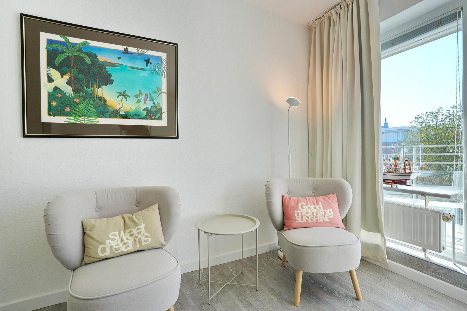 Zwei Sessel mit Kissen, Tisch und Wandbild. Blick auf Balkon mit Boot.