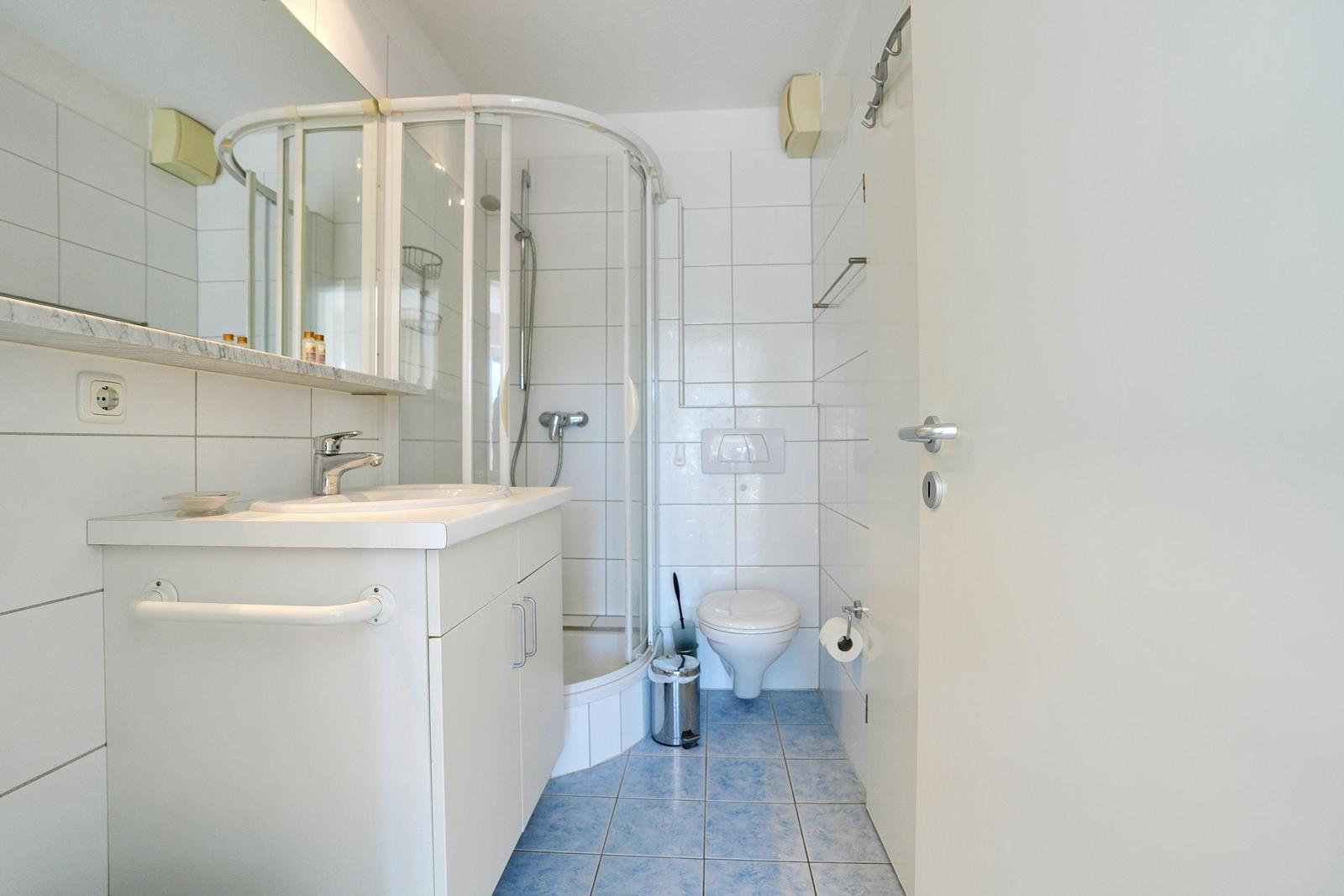 Badezimmer mit Dusche, Waschbecken und Toilette. Fliesenboden und Spiegel.
