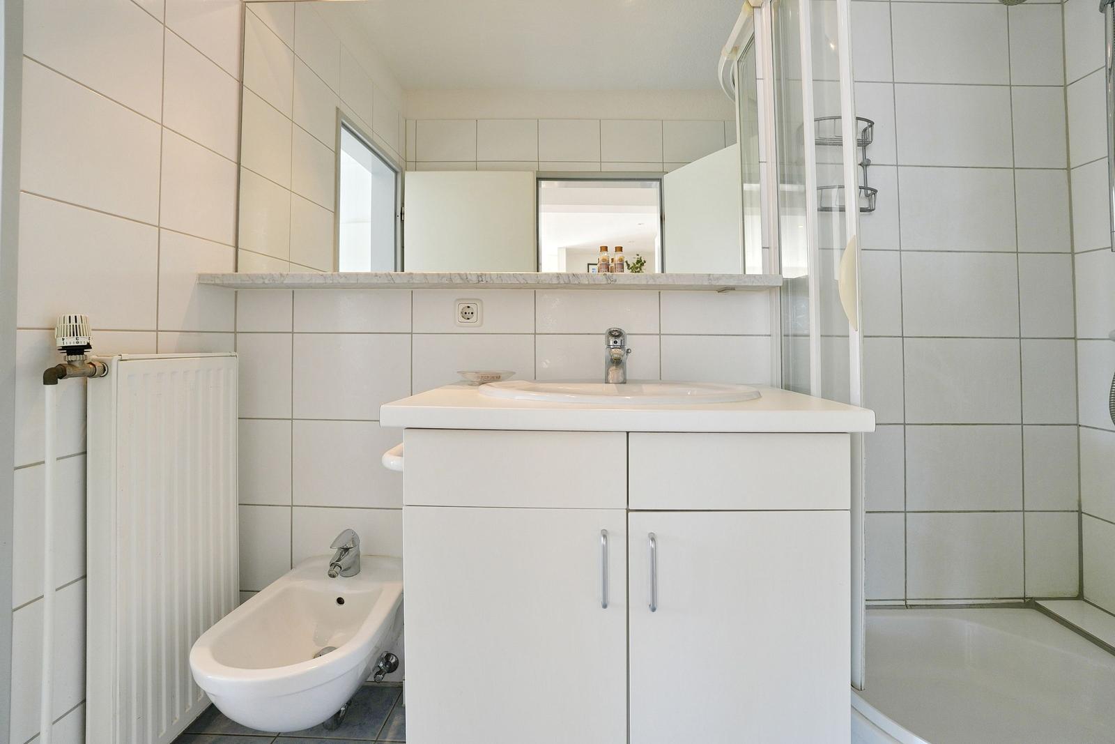 Badezimmer mit Waschbecken, Dusche und Bidet. Weiße Fliesen und Spiegelschrank.