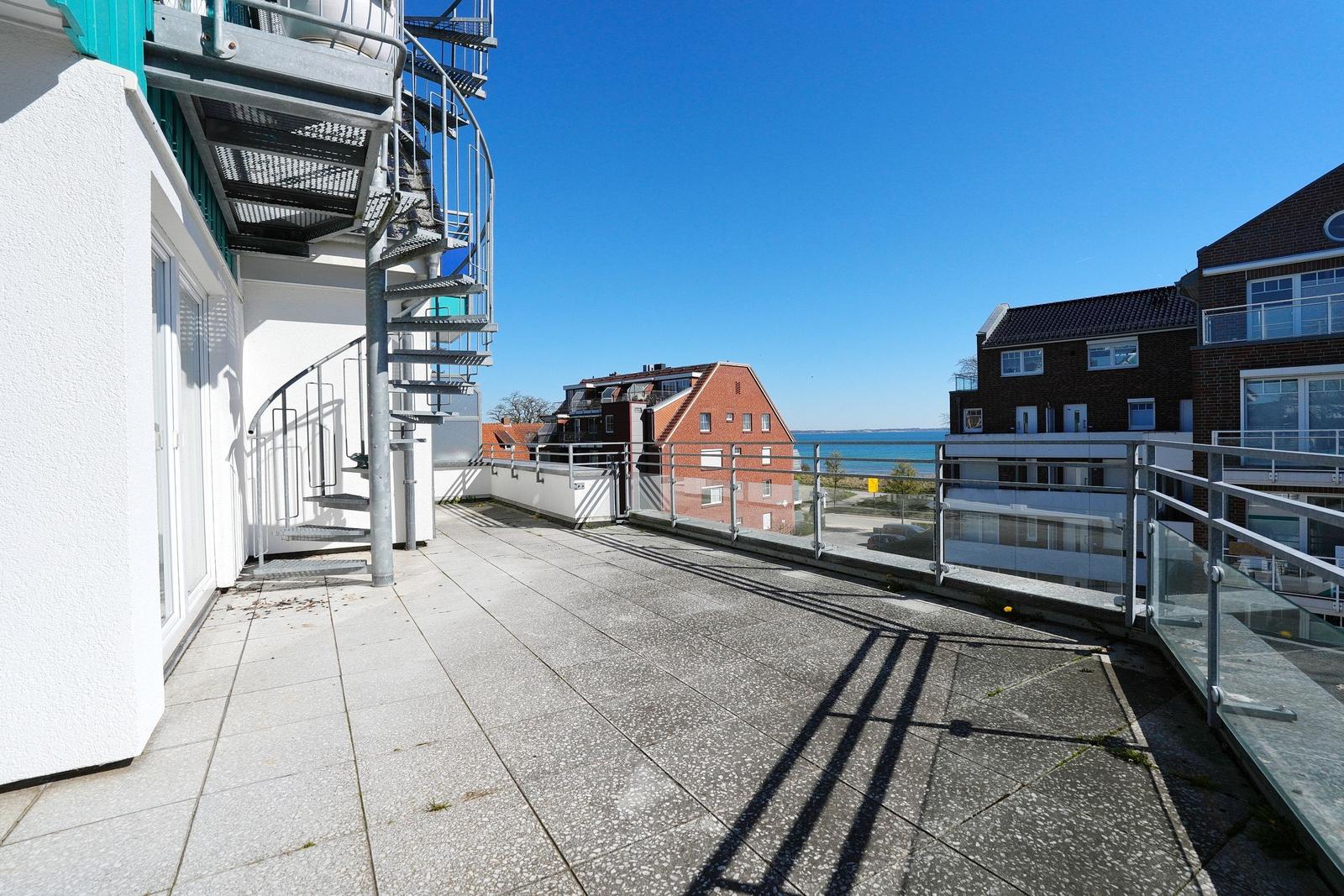 Terrasse mit Blick auf den Hafen und benachbarte Gebäude unter blauem Himmel.
