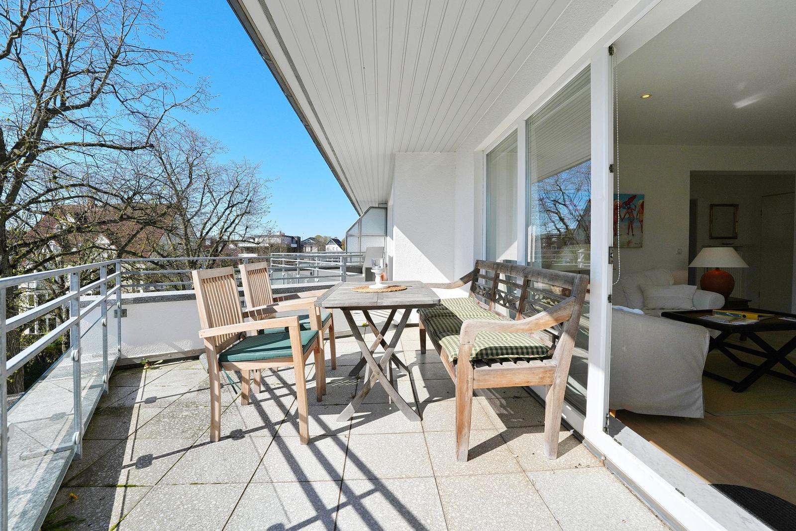 Terrasse mit Tisch, Stühlen und Bank. Blick auf Bäume und Wohnraum.