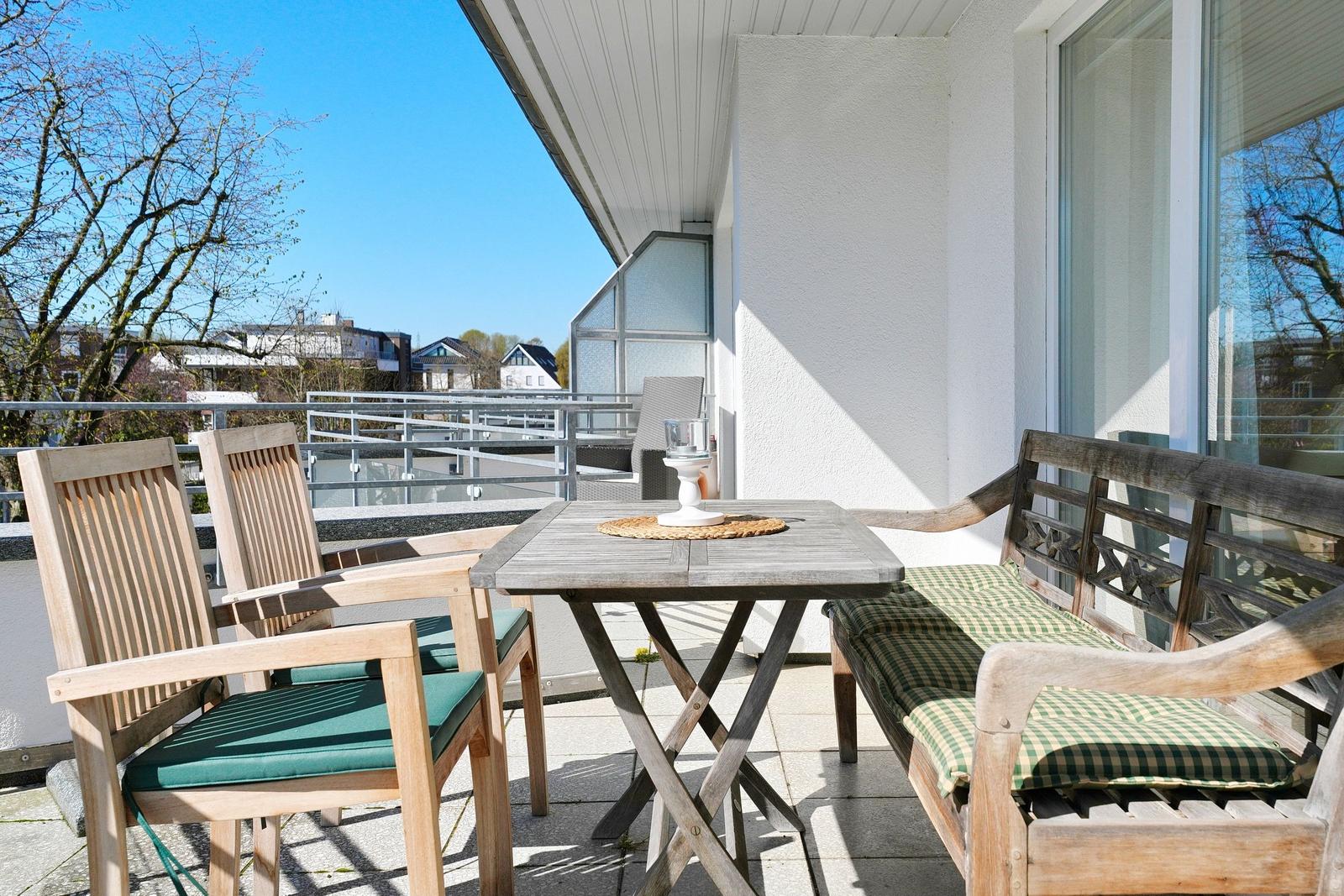 Terrasse mit Holztisch, zwei Stühlen und einer Bank mit Kissen.