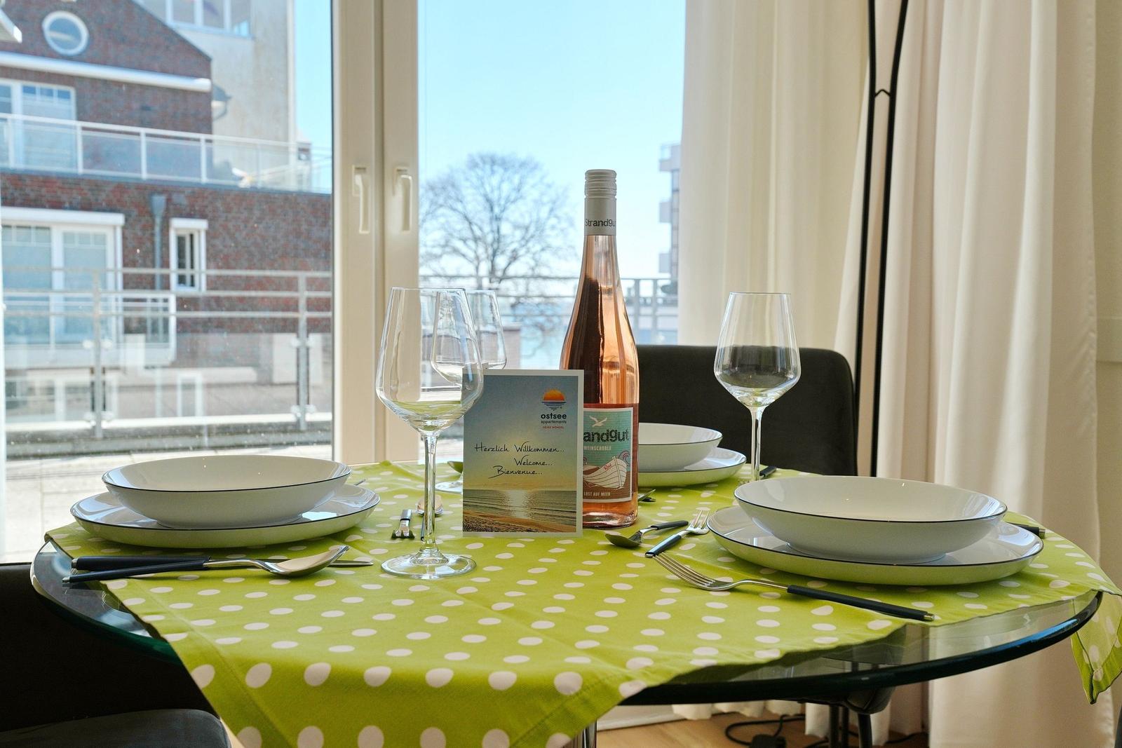 Tisch mit Tischdecke, Gläsern und Flasche vor Fenster mit Blick auf Gebäude.
