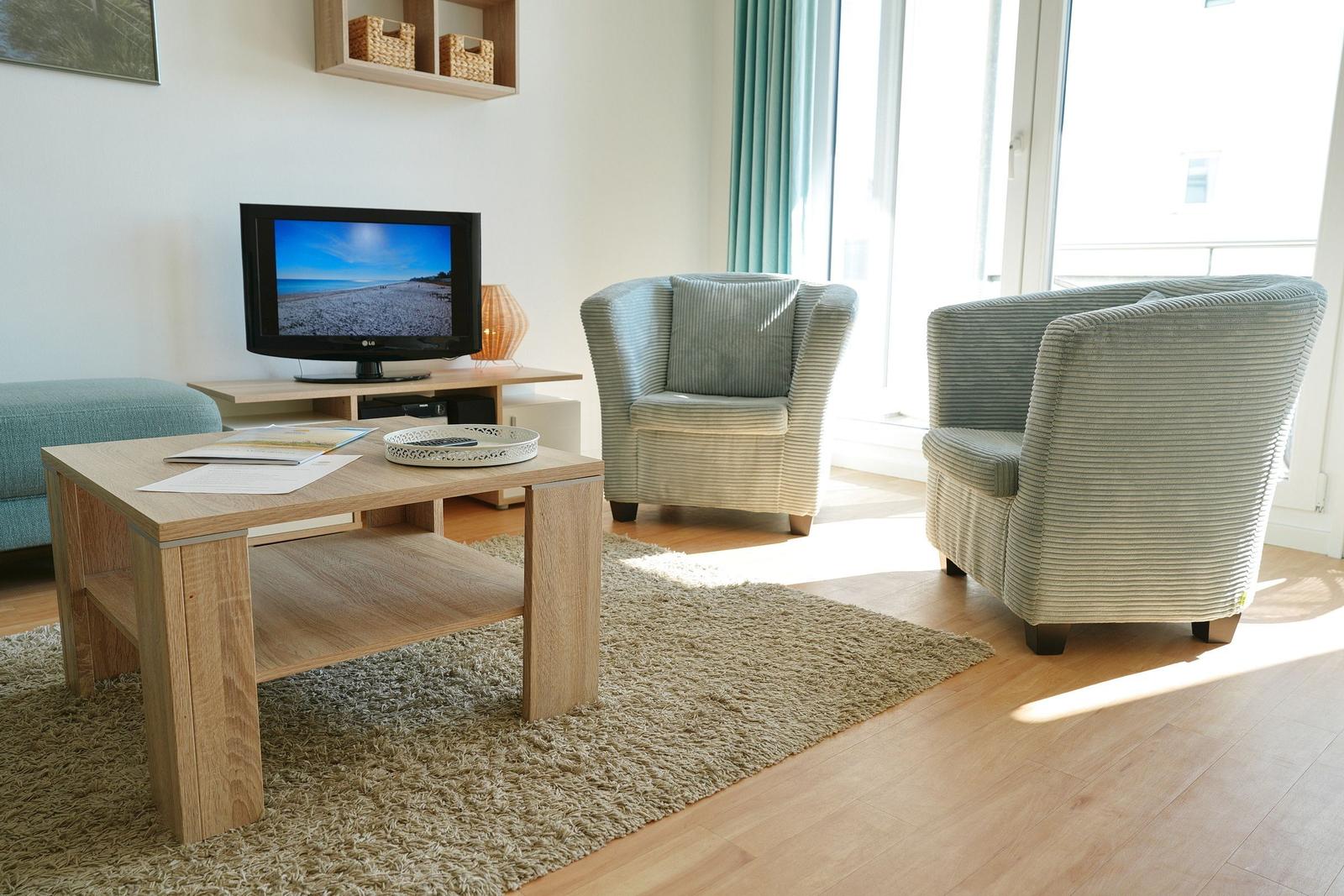 Wohnzimmer mit zwei Sesseln, Couchtisch und Fernseher. Licht durch Fenster.