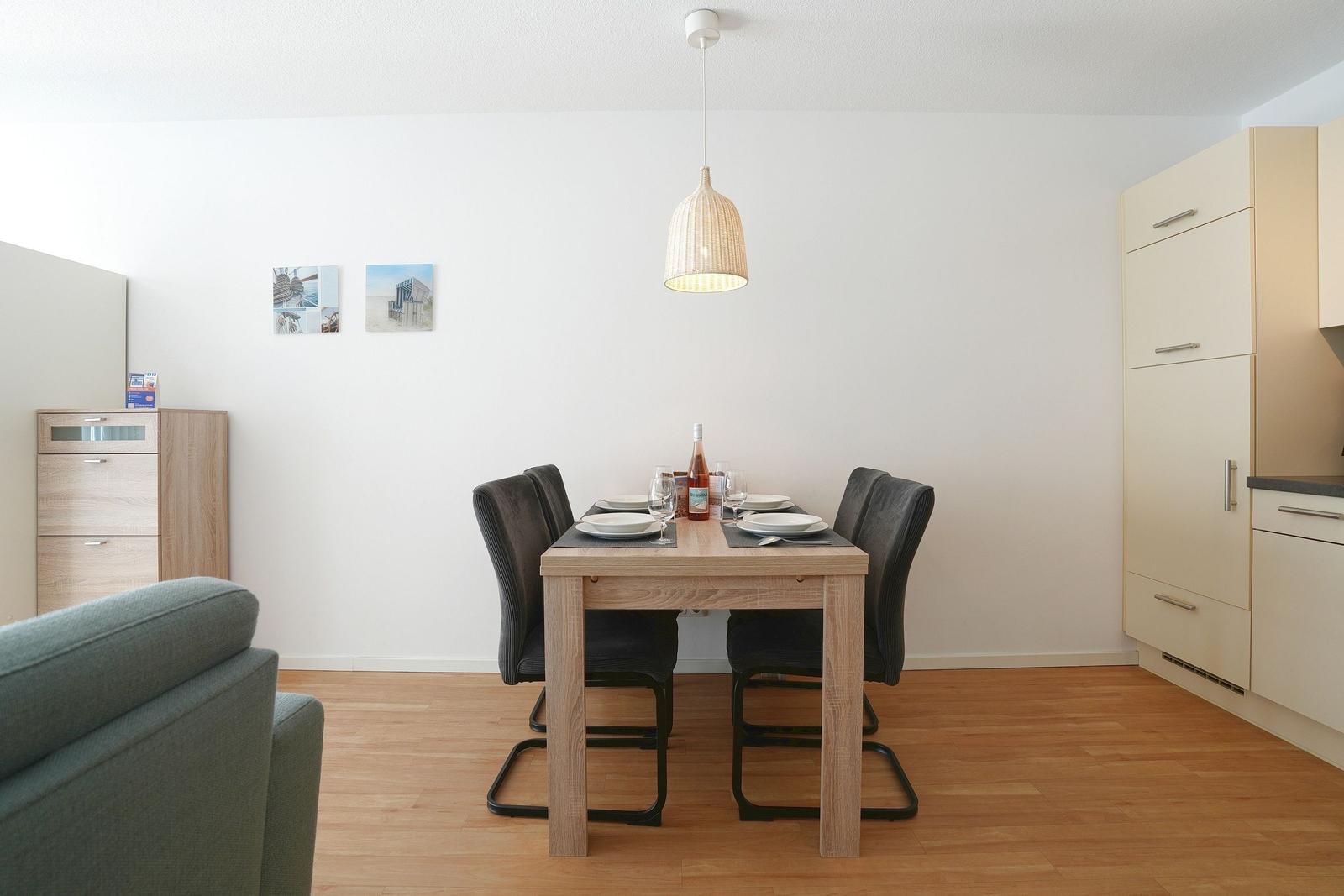 Essbereich mit Holztisch, vier Stühlen und Pendelleuchte. Küche und Wohnbereich sind sichtbar.