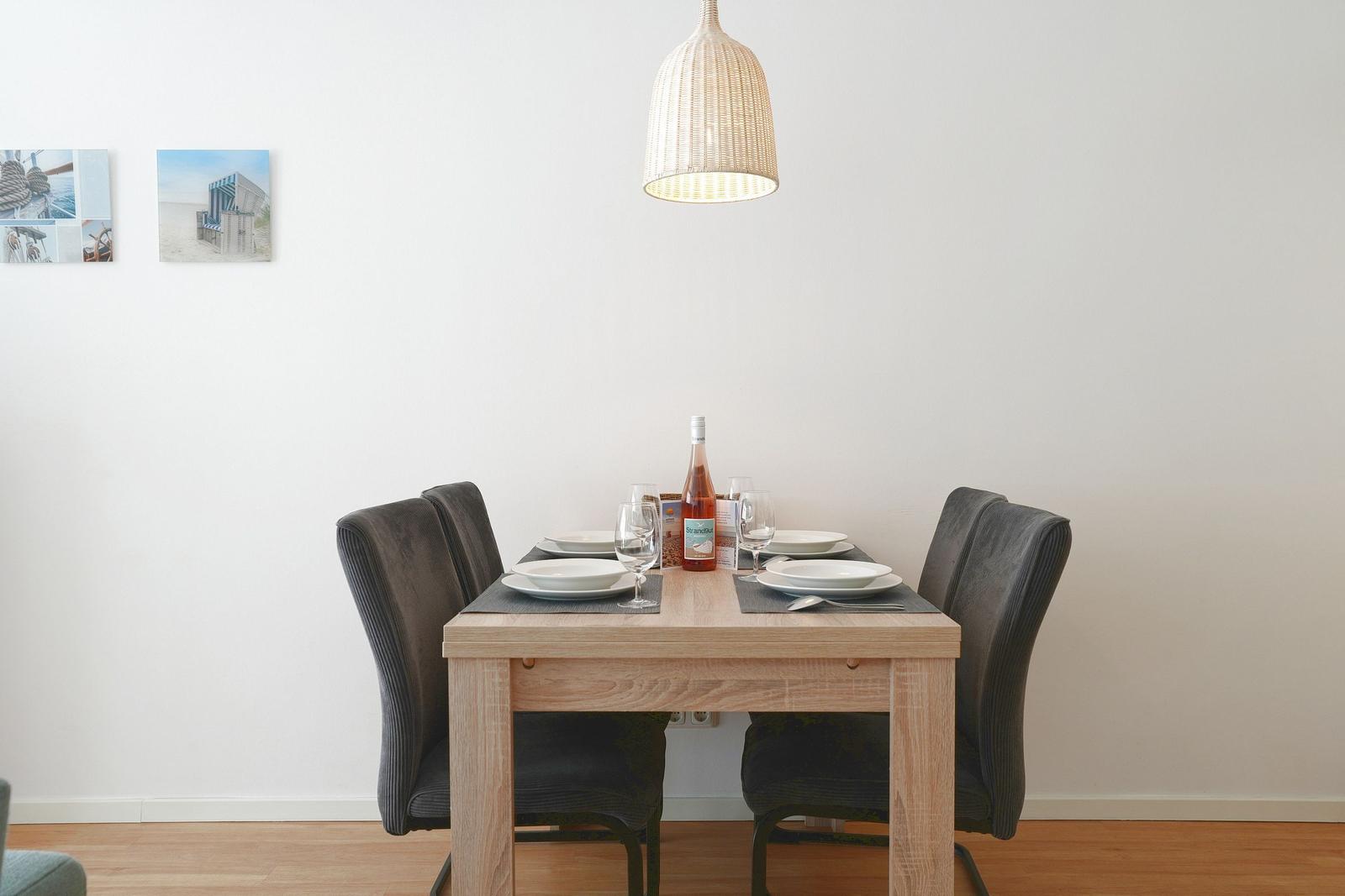 Esszimmer mit Holztisch, vier Stühlen und Pendelleuchte. Wandbilder zeigen Strandmotiv.