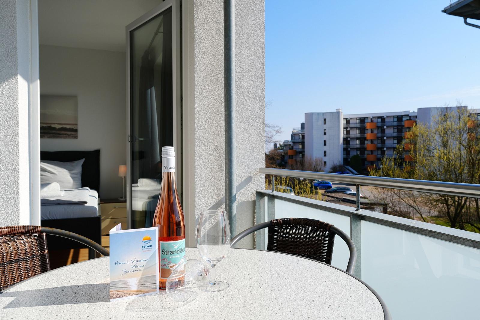 Terrasse mit Tisch, Stühlen und Wein. Blick auf Gebäude und Bäume.