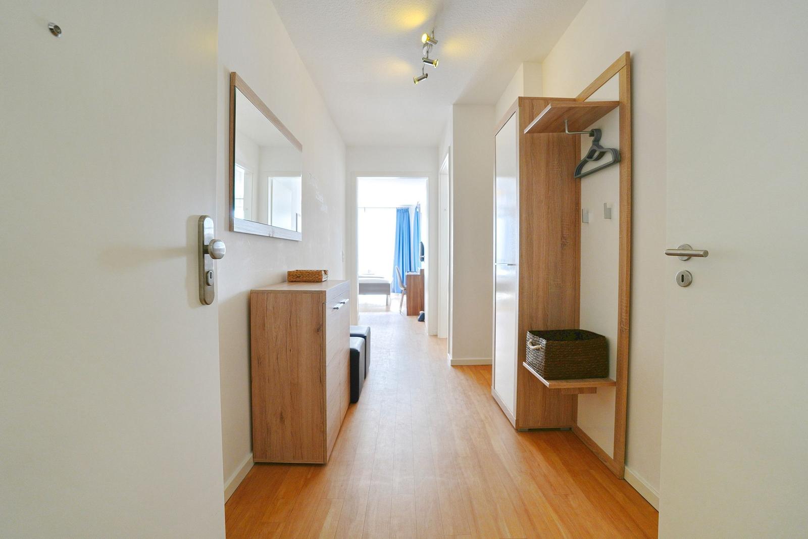 Flur mit Holzboden, Spiegelschrank und Kleiderständer. Durchgang zur Schlafzimmer.
