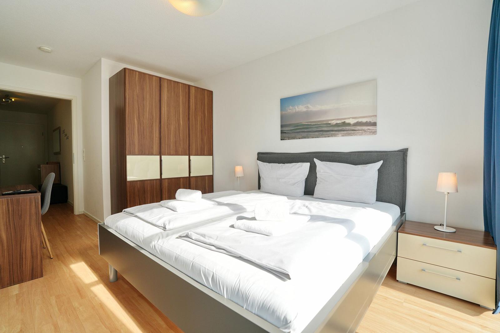 Schlafzimmer mit Doppelbett, Kleiderschrank und Nachttisch. Wandbild zeigt Wellen.