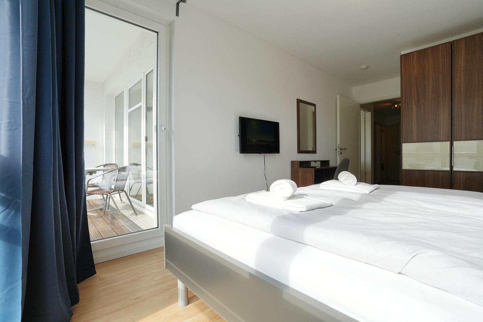 Schlafzimmer mit Doppelbett, TV und Balkon. Holzboden und Schwebetüren.