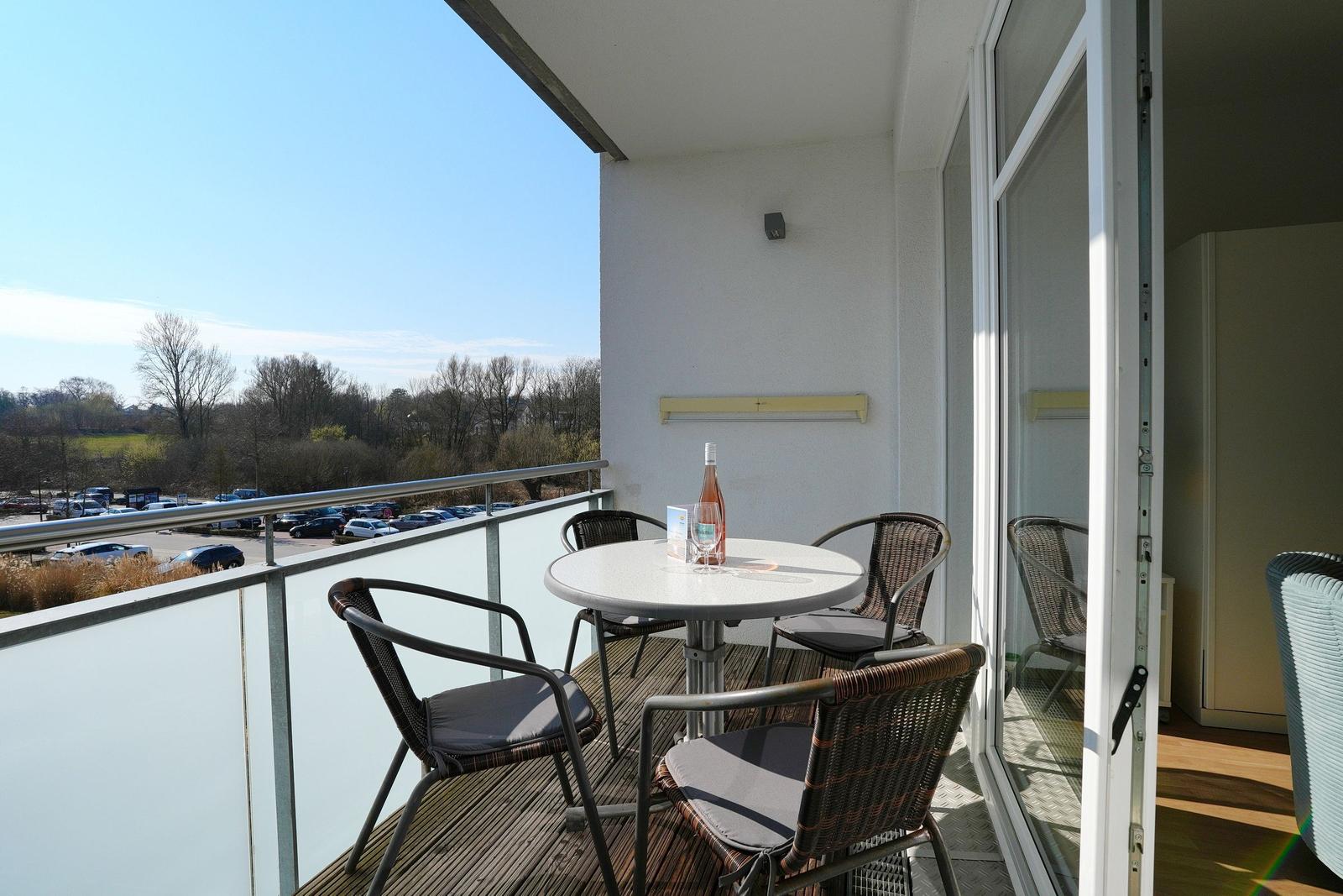 Terrasse mit Tisch und Stühlen, Blick auf Parkplatz und Bäume.