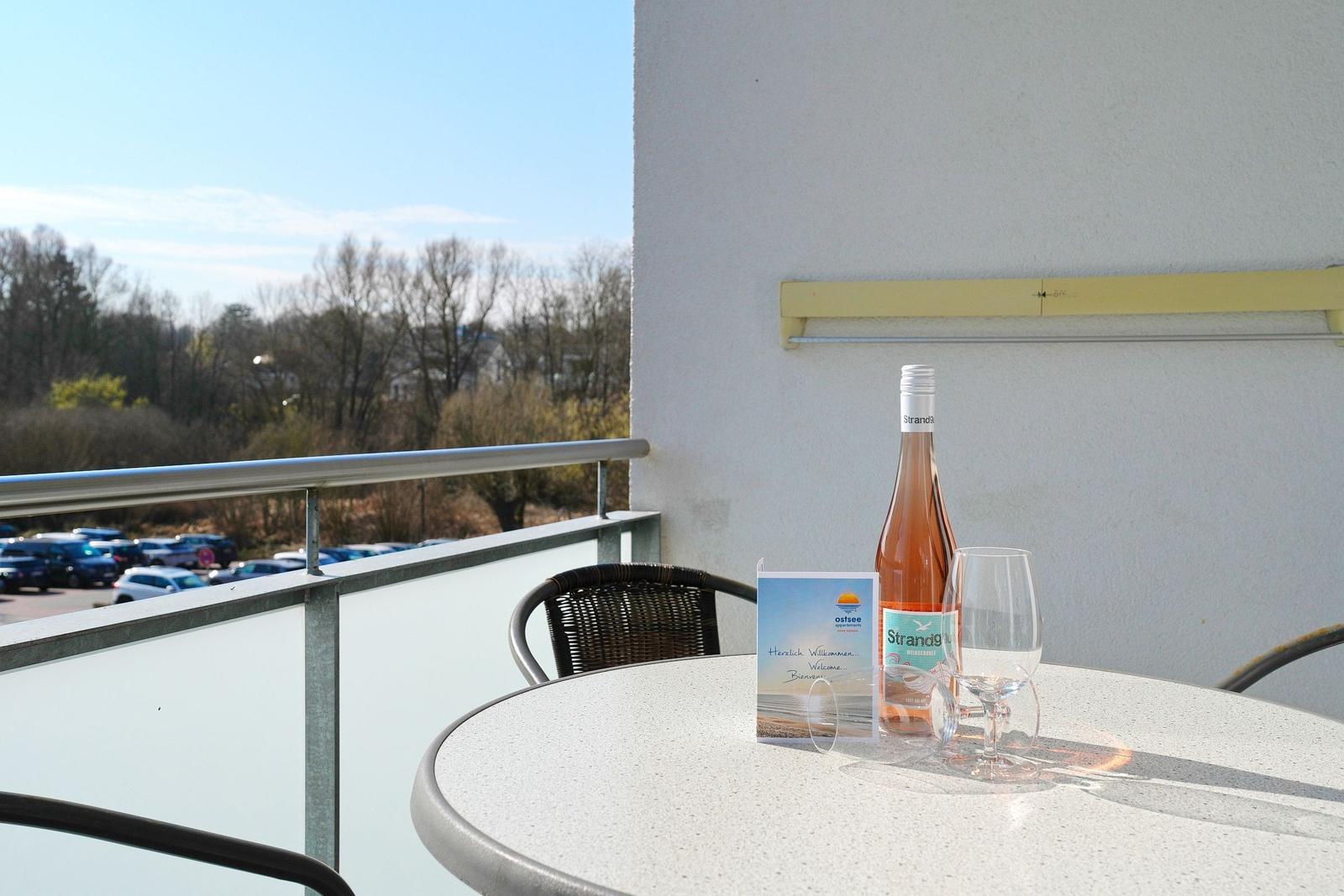 Terrasse mit Tisch, Stühlen, Flasche und Glas. Blick auf Parkplatz und Bäume.