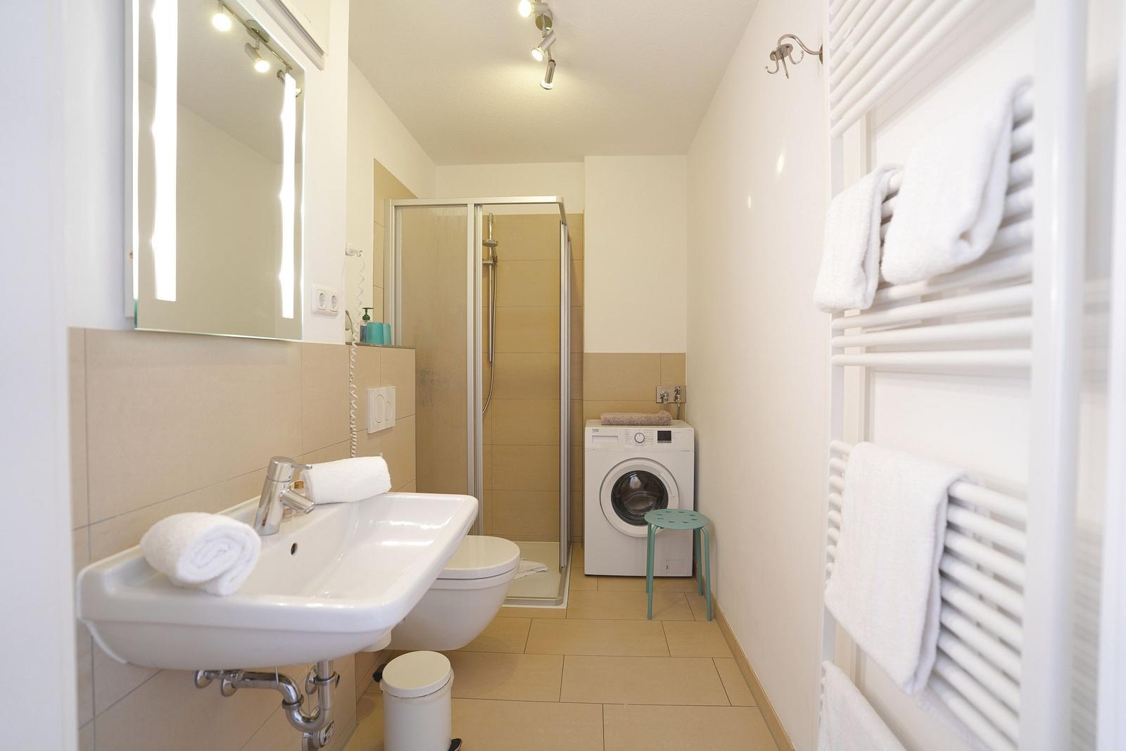 Badezimmer mit Dusche, Waschmaschine und Heizkörper mit Handtüchern.