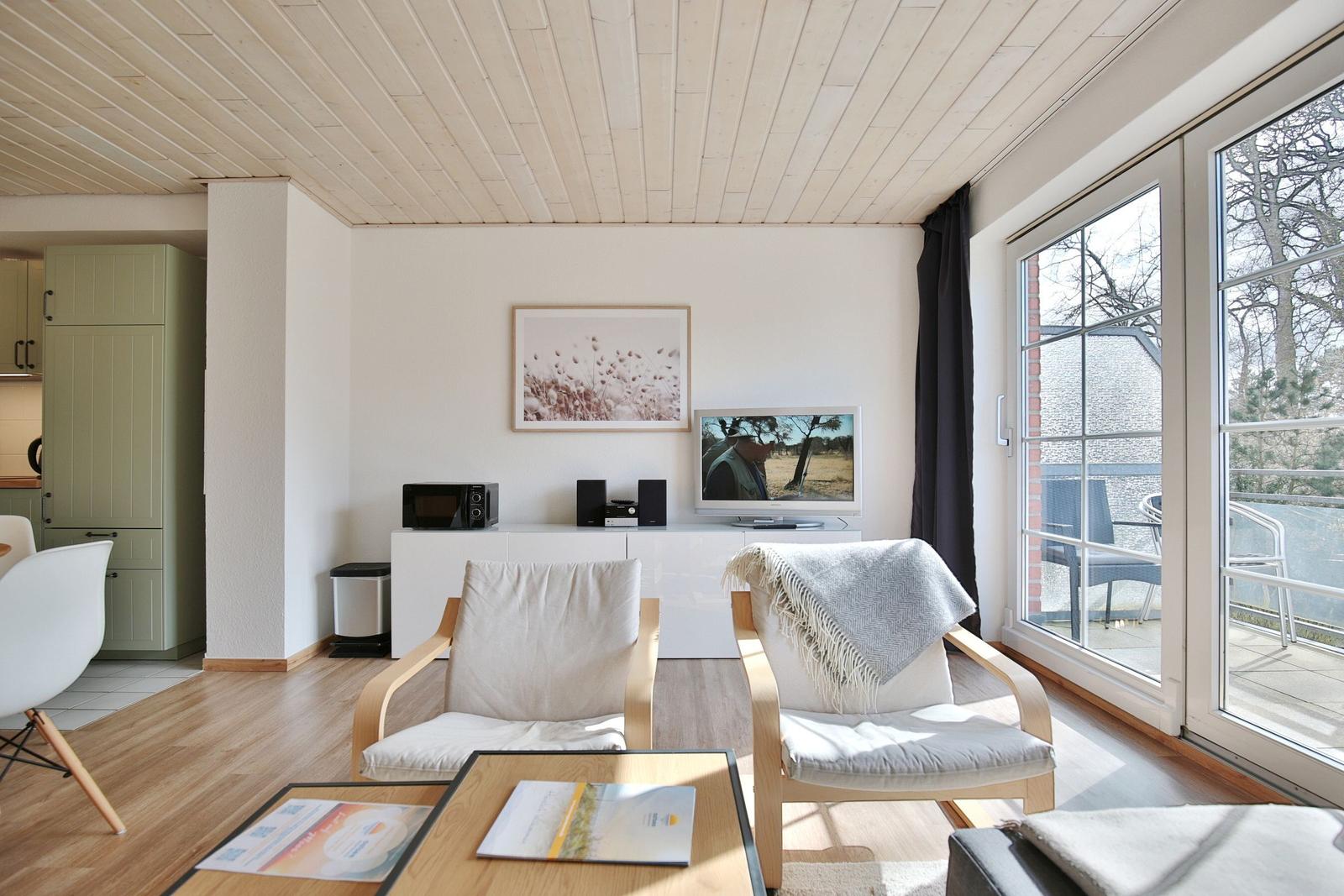 Wohnzimmer mit zwei Sesseln, Fernseher und Blick auf Balkon.
