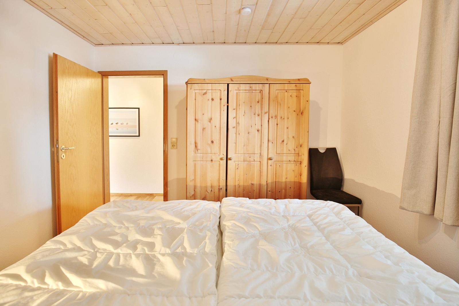 Schlafzimmer mit Doppelbett, Holzschrank und Stuhl. Decke aus Holzplanken.