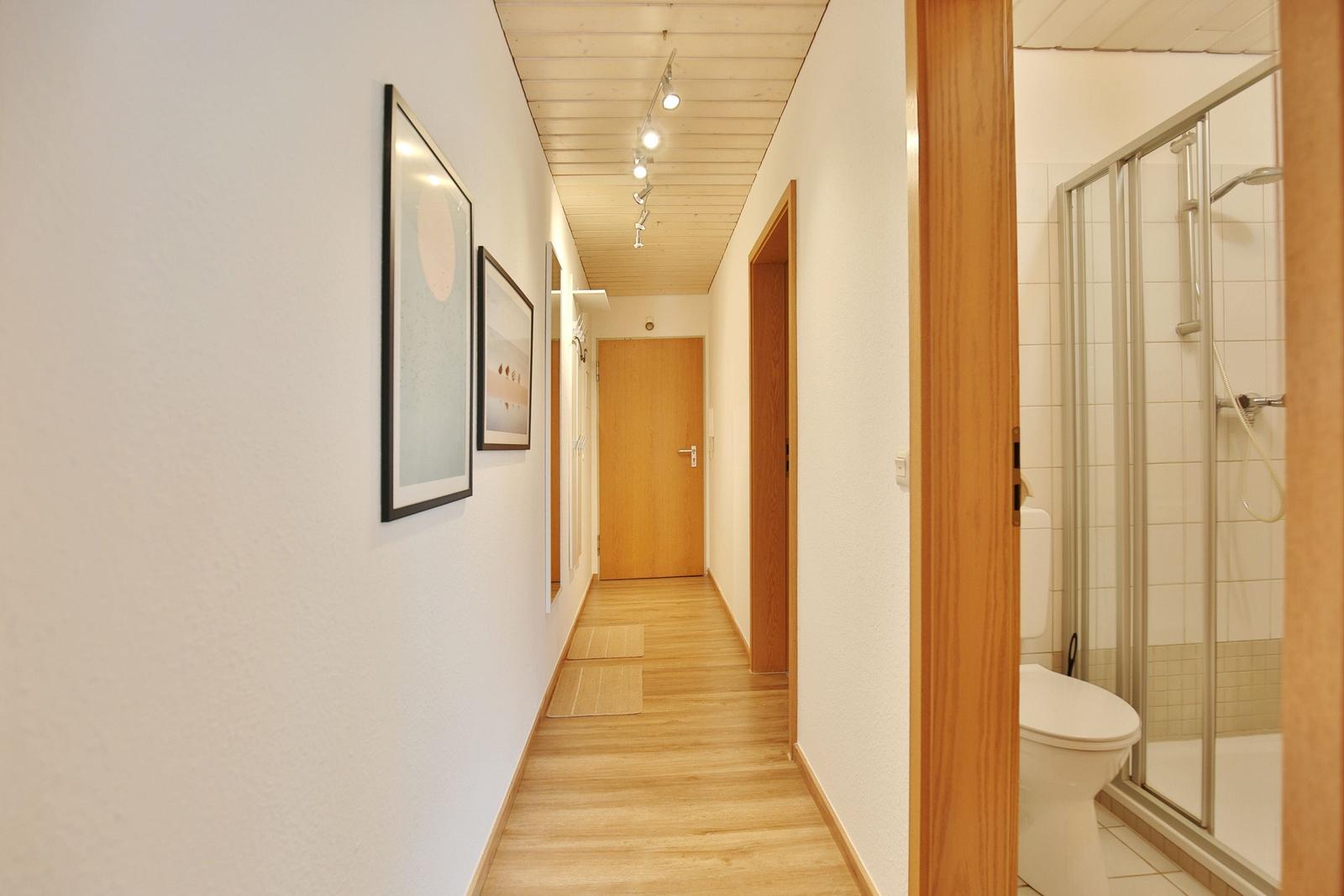 Flur mit Holzboden, Bildern an der Wand und Blick in die Badewanne.
