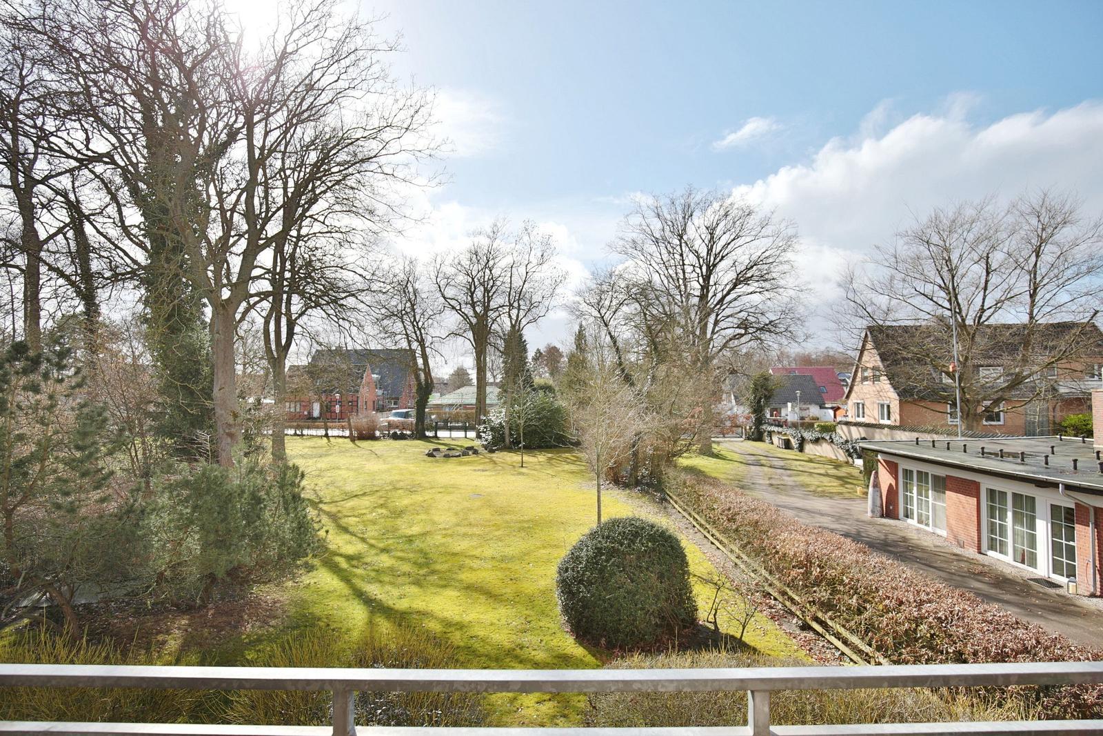 Grüner Rasenbereich mit Bäumen und einem Gartenhaus im Hintergrund.