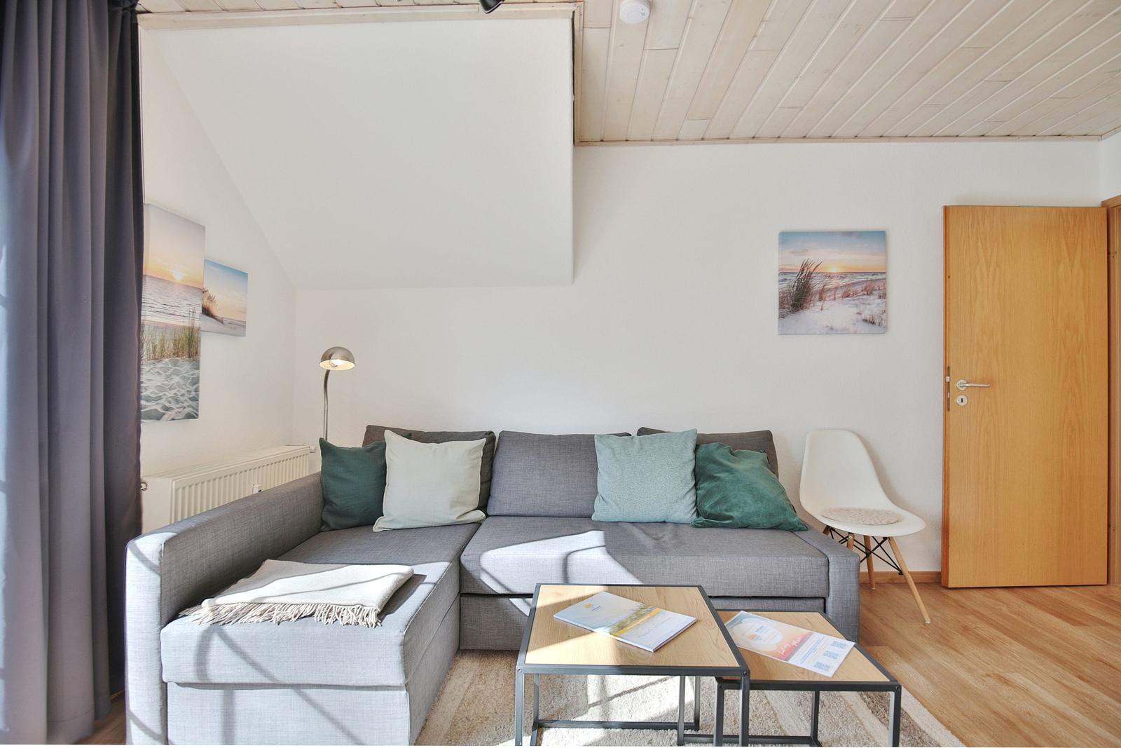 Wohnzimmer mit grauem Sofa, Holzfußboden und Wandbildern.