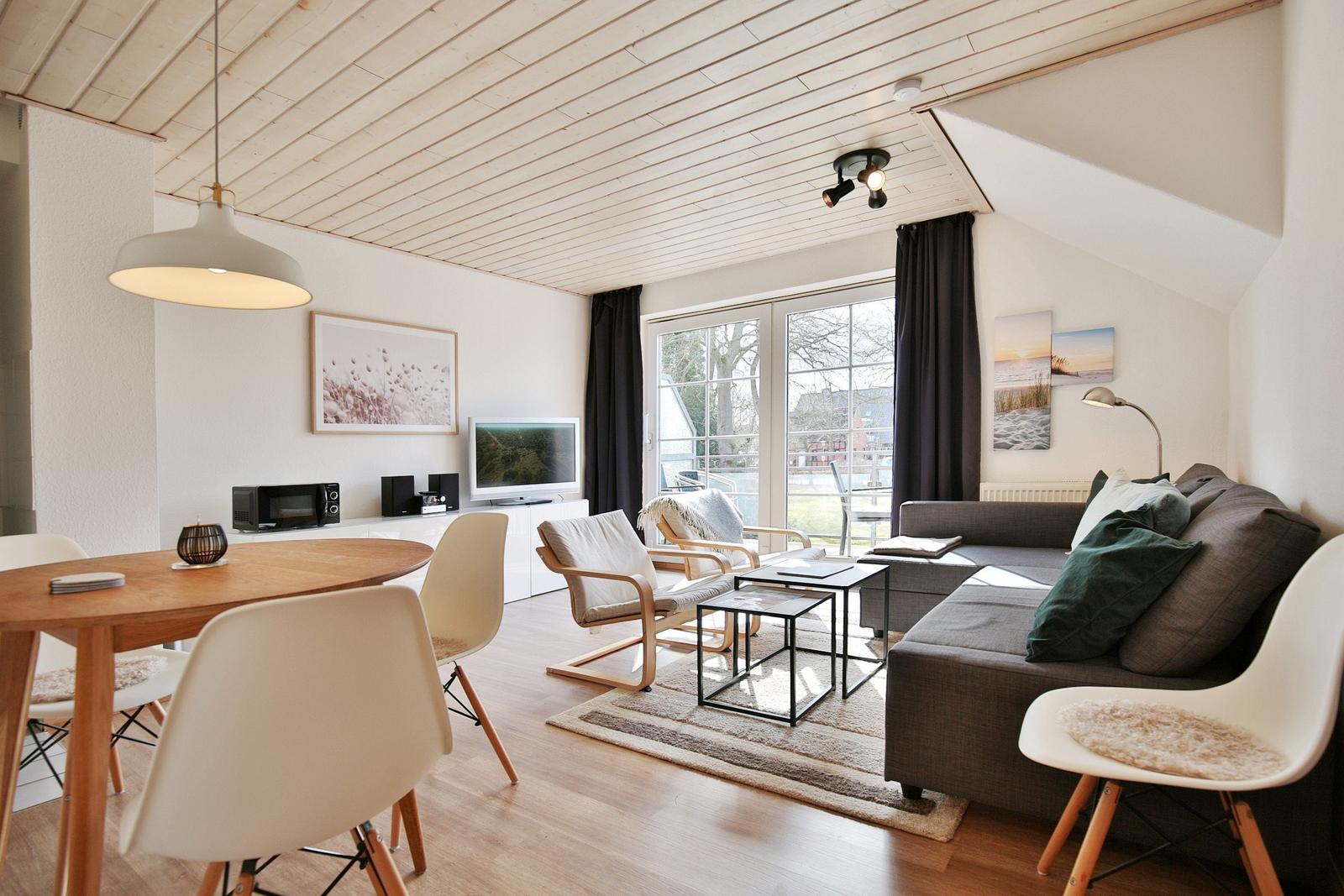 Wohn- und Essbereich mit Sofa, Stühlen, TV und Fenster zur Terrasse.
