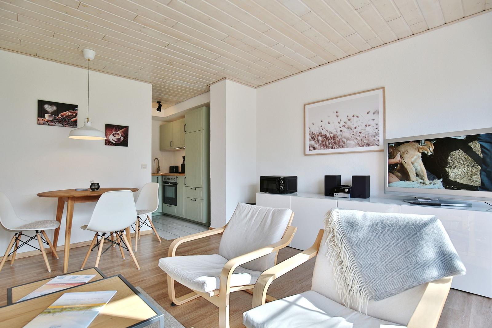 Wohnbereich mit Essplatz, Küche und Fernseher. Holzdecke und weiße Wände.