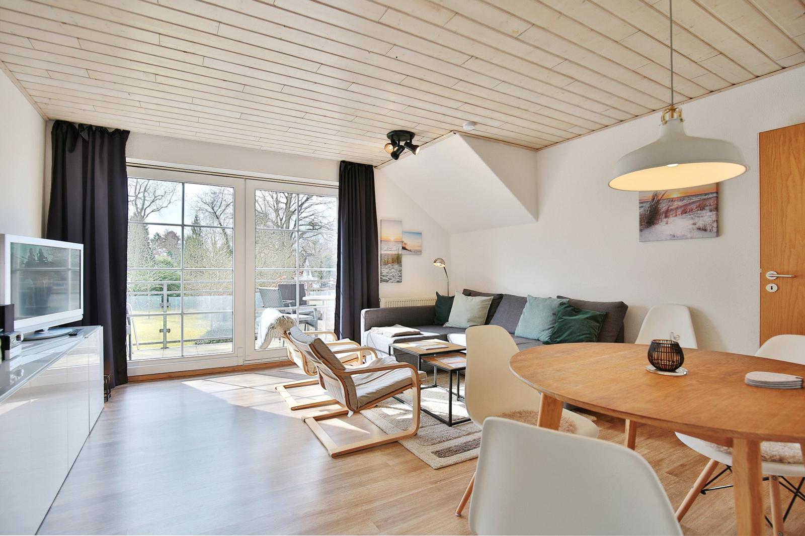 Wohn- und Essbereich mit Holzdecke, Sofa, Esstisch und Balkontür.