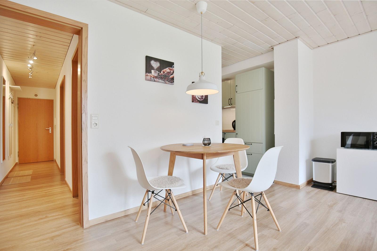 Essbereich mit runden Tisch und weißen Stühlen. Hintergrund zeigt Küchenbereich und Flur.