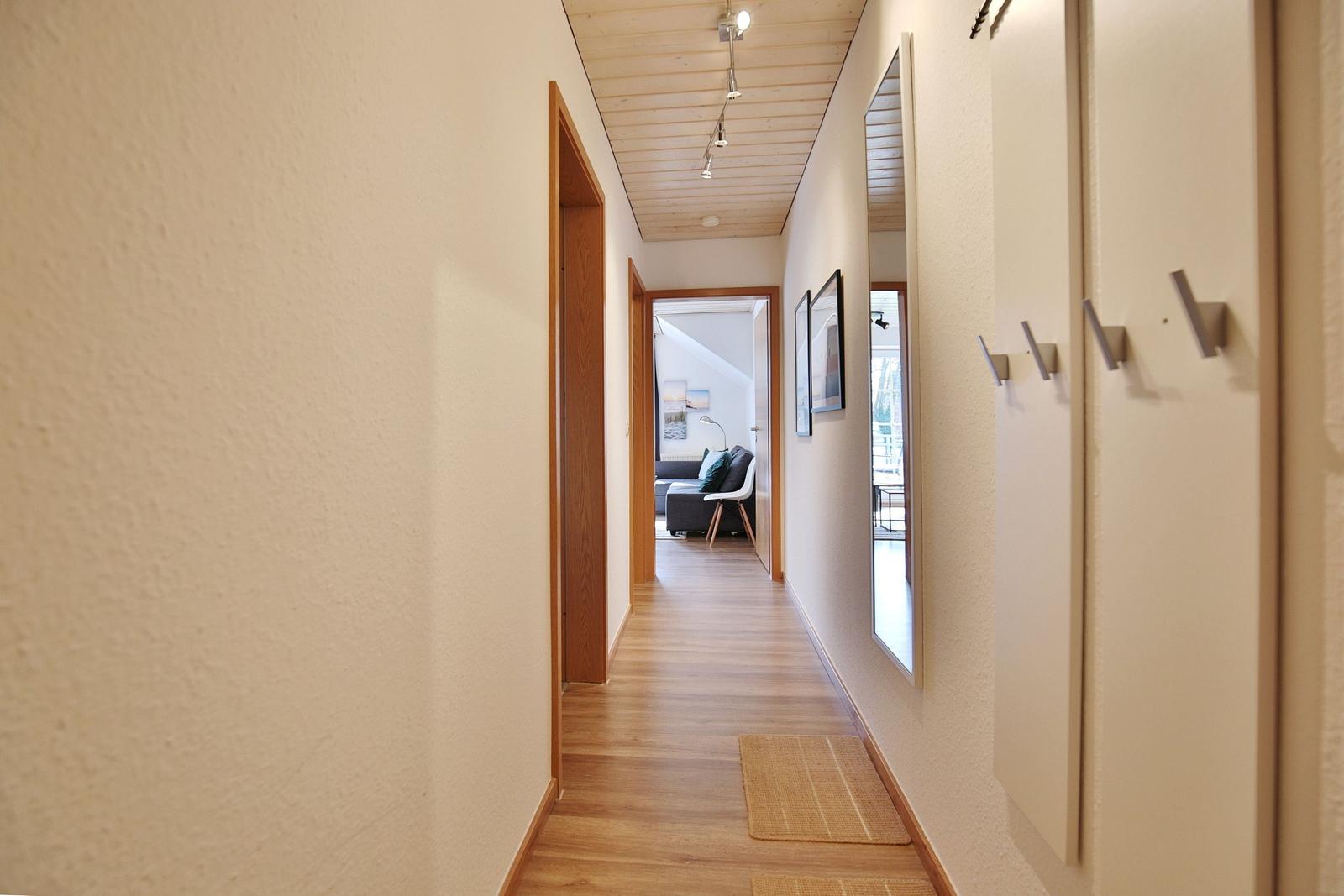 Flur mit Holzboden und Türen, Blick in Wohnzimmer mit Sofa und Stuhl.