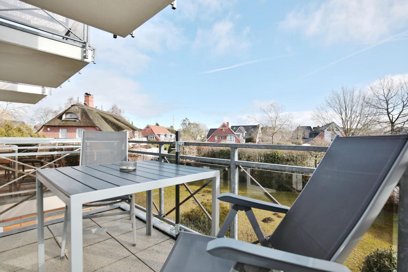 Terrasse mit Tisch und Liegestuhl. Blick auf Dächer und Bäume.