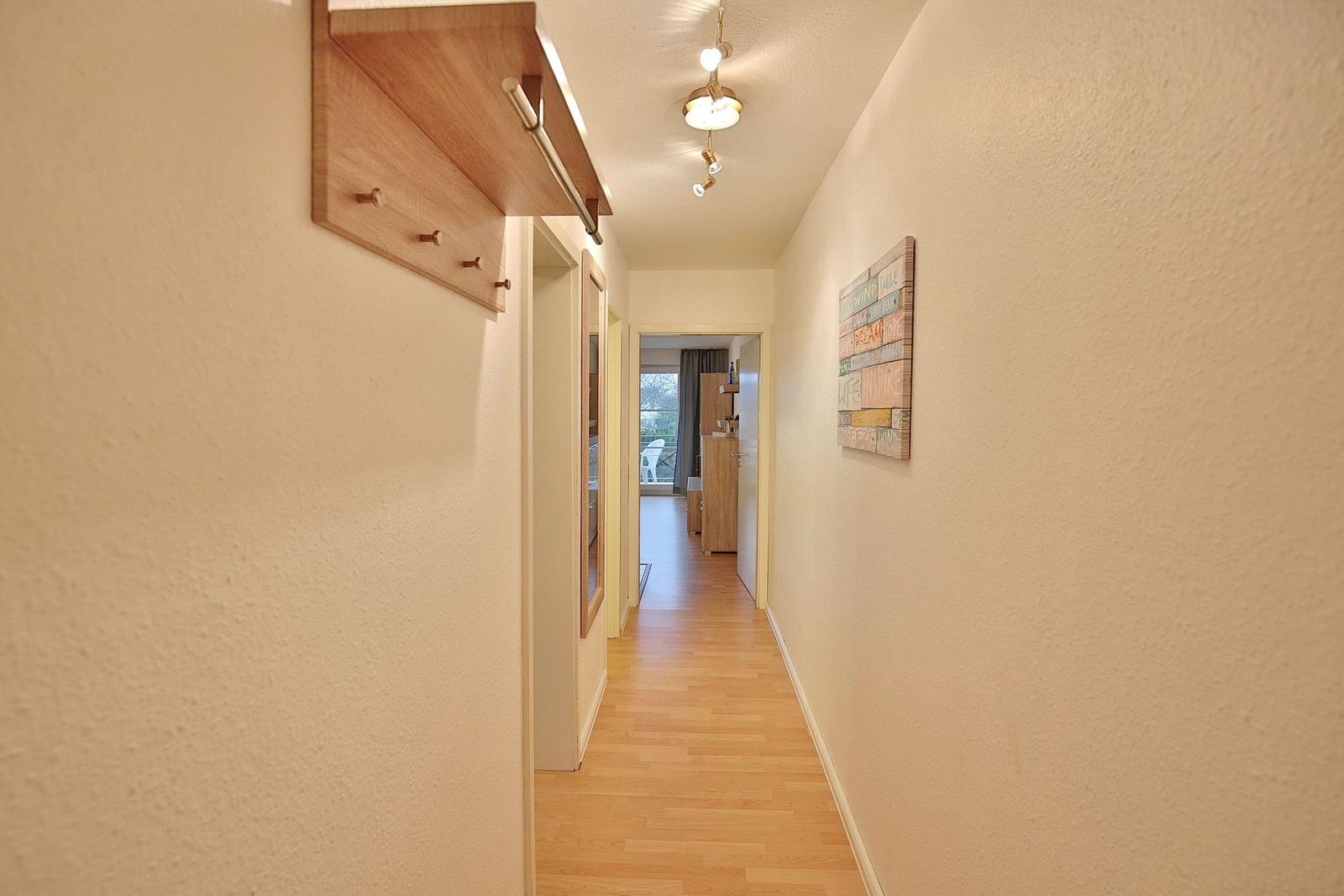 Flur mit Holzboden, Wandregal und Bild an der Wand. Durchgang zu Küche und Balkon.