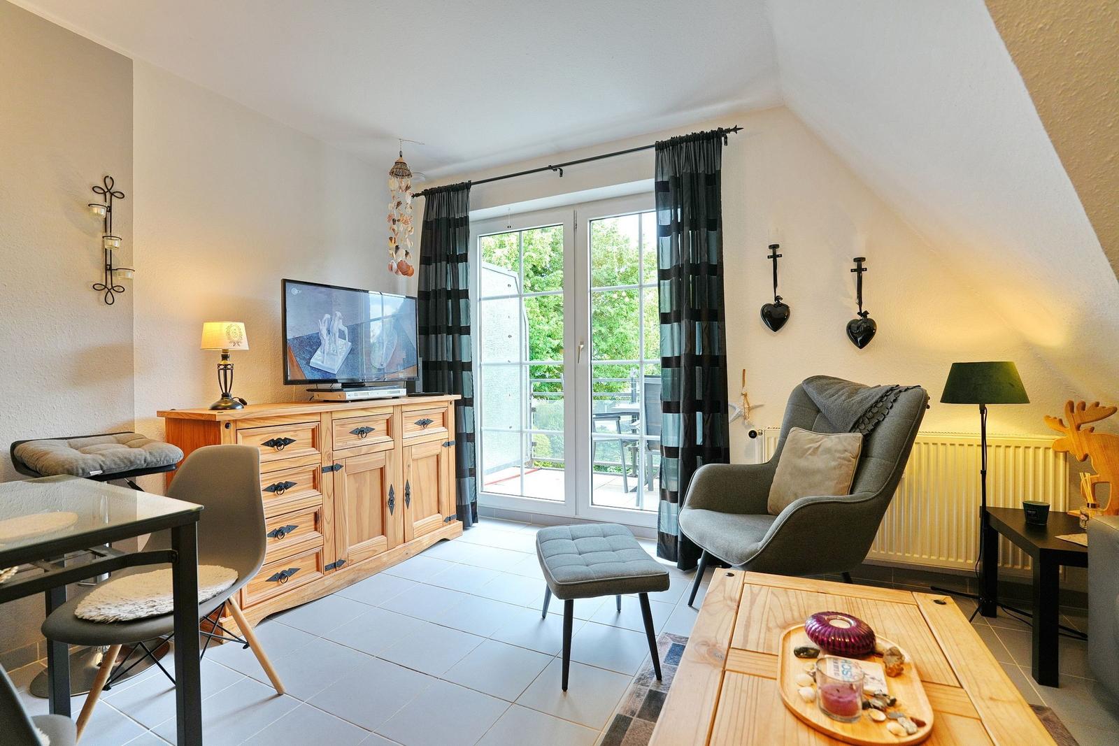 Wohnzimmer mit TV, Sitzgelegenheiten und Balkonzugang.