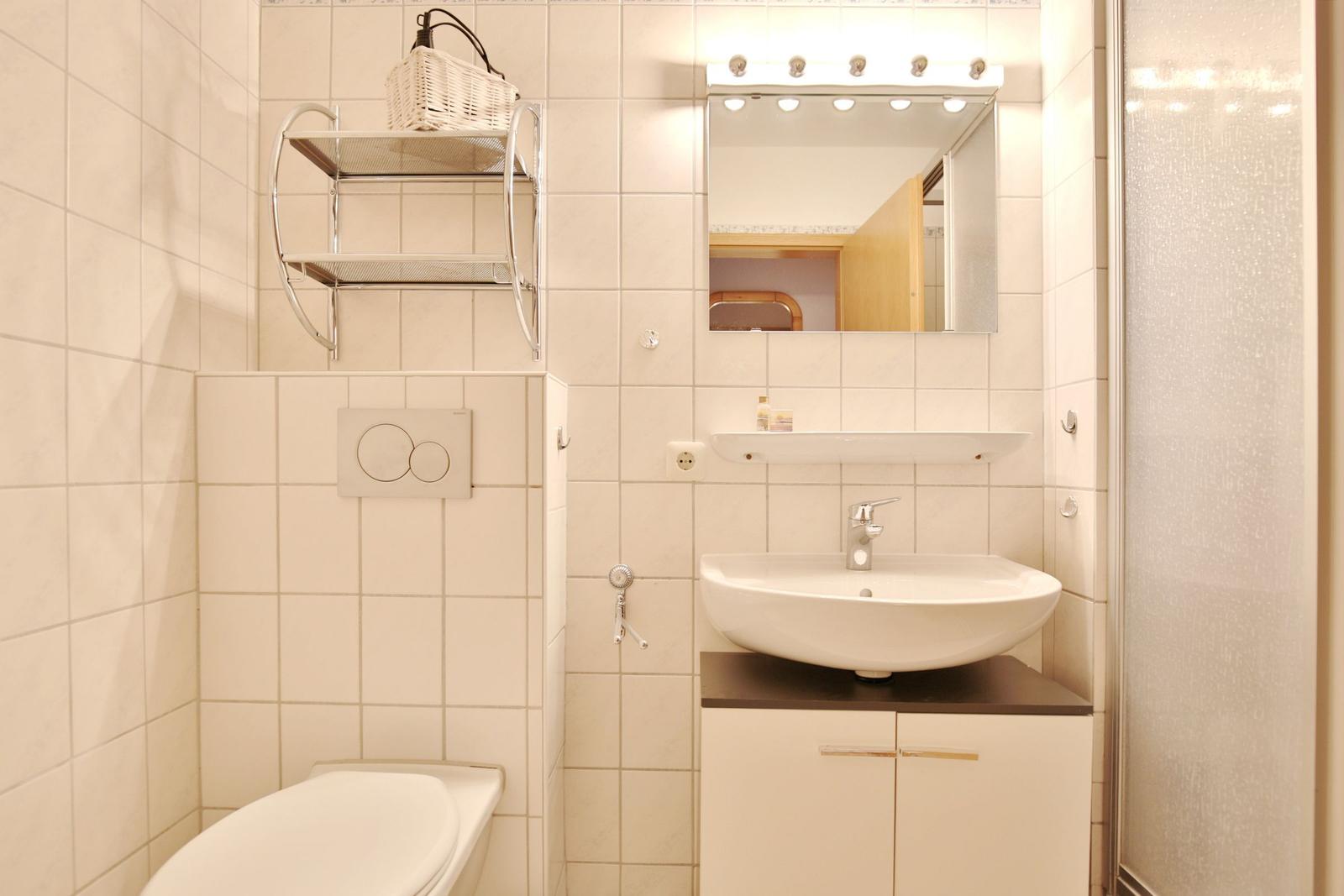 Badezimmer mit Waschbecken, Spiegel, Toilette und Dusche.