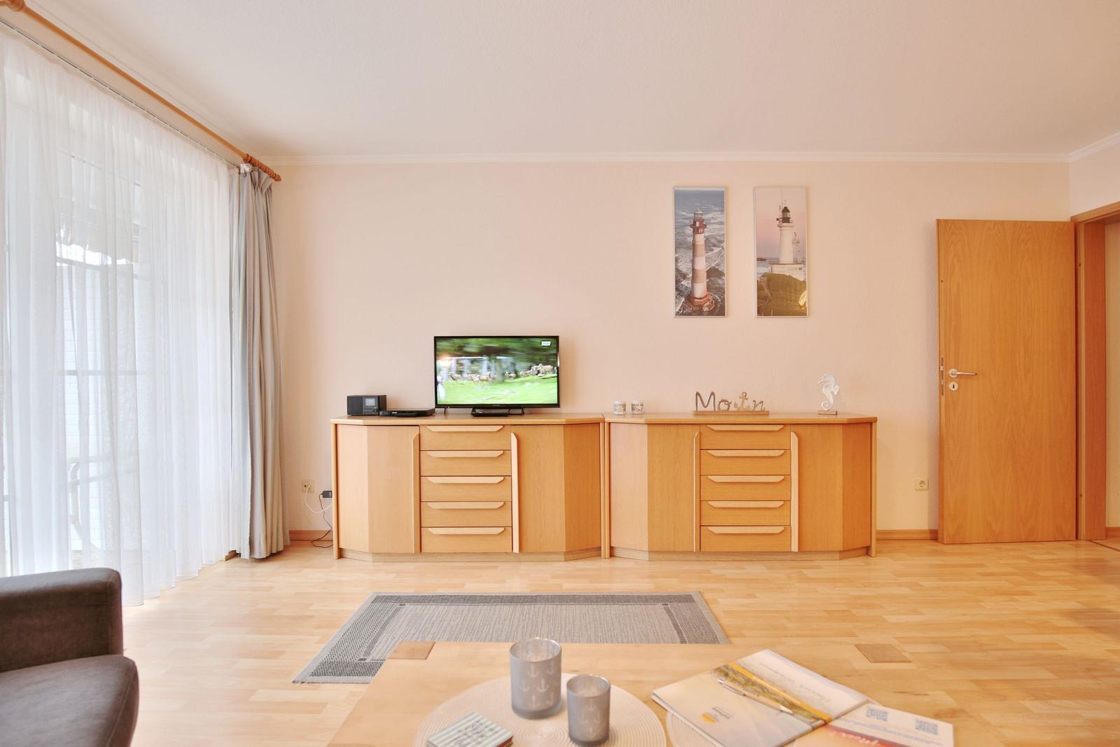 Wohnzimmer mit Holzmöbeln, Fernseher und Lichteinblick.