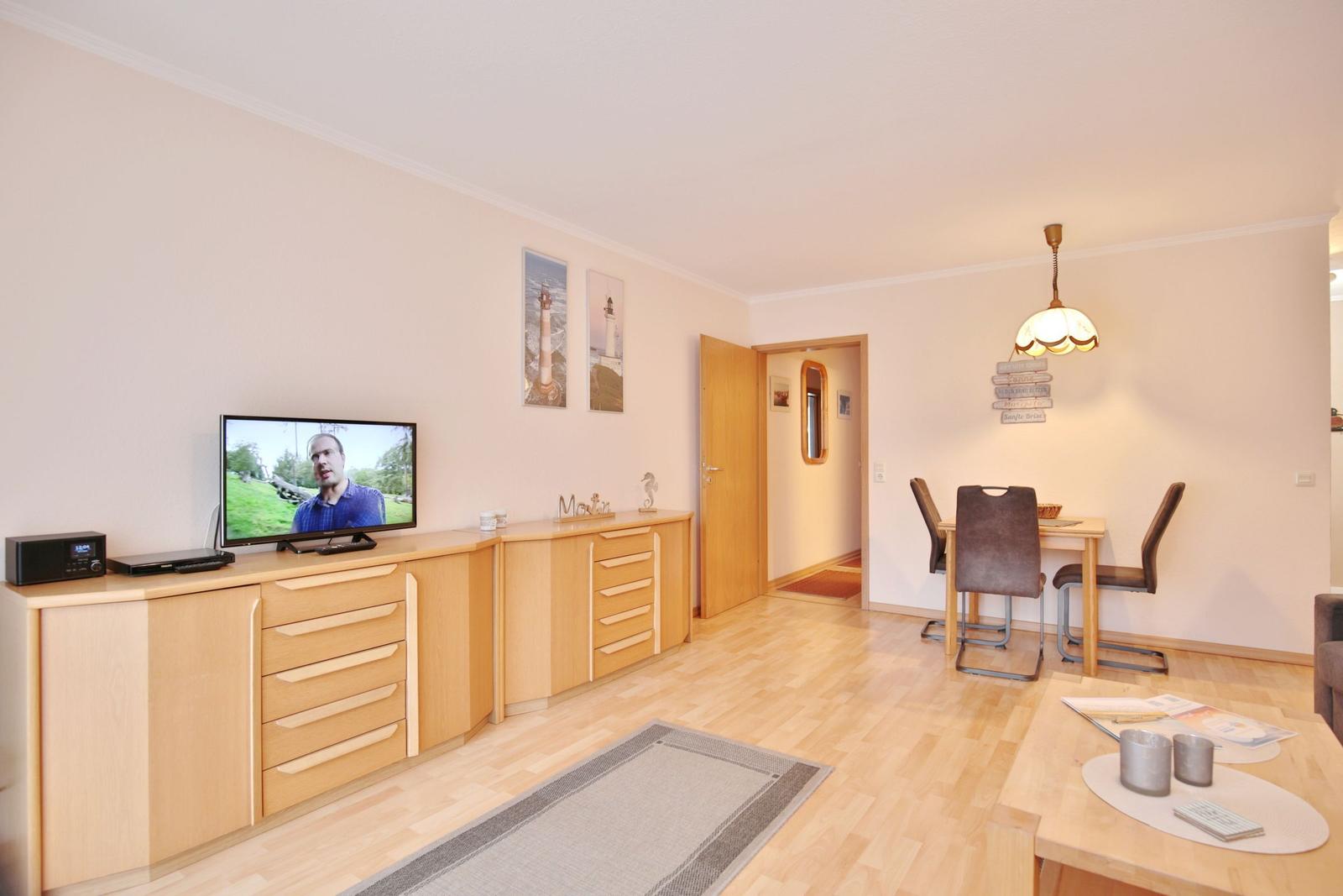 Wohn- und Essbereich mit TV, Holzmöbeln und Lichtdecke.