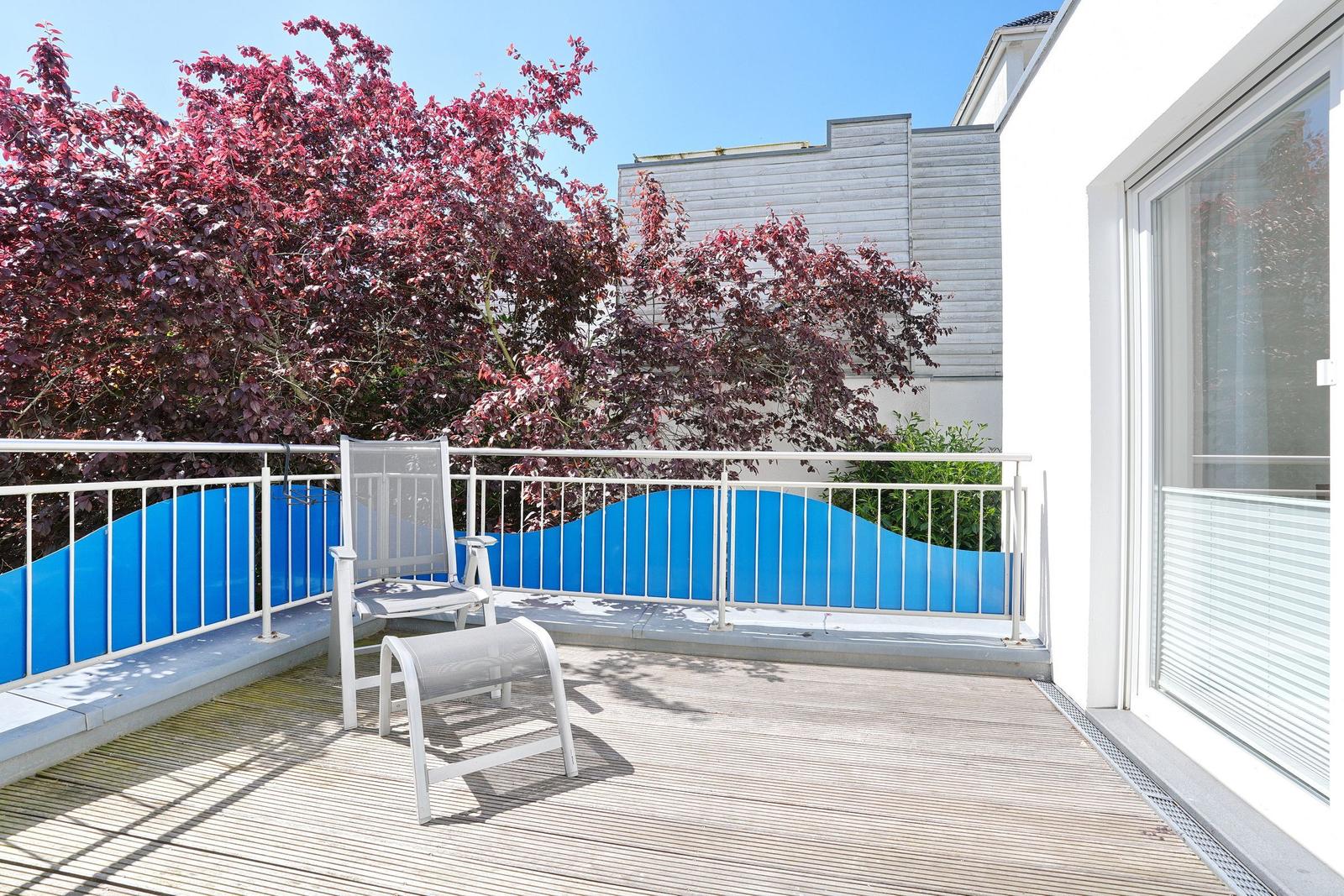 Terrasse mit Stuhl, blauer Geländer und rotem Baum.