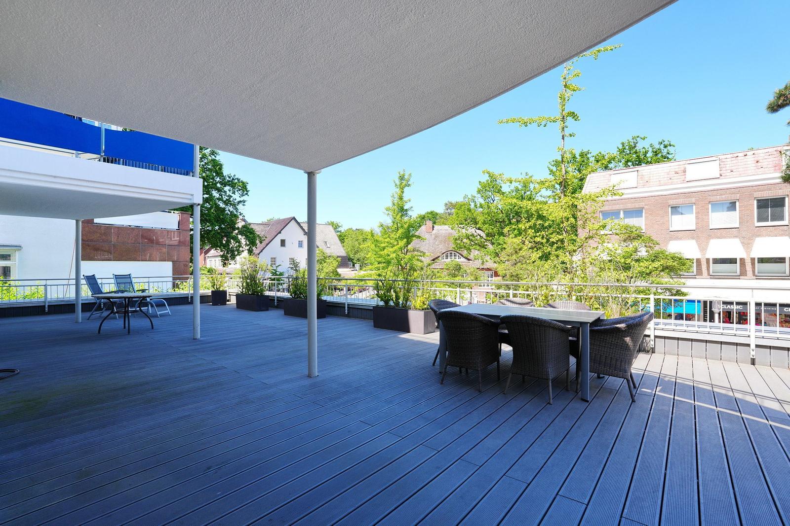 Terrasse mit Tisch und Stühlen unter Markise. Blick auf Grün und Gebäude.