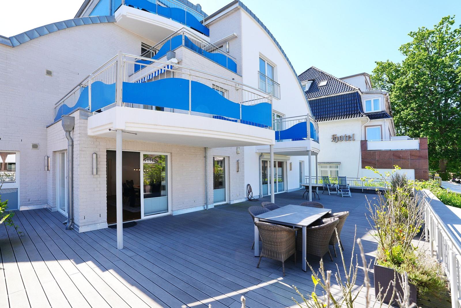 Hotel mit Terrasse, blauen Balkonen und Tisch mit Stühlen.