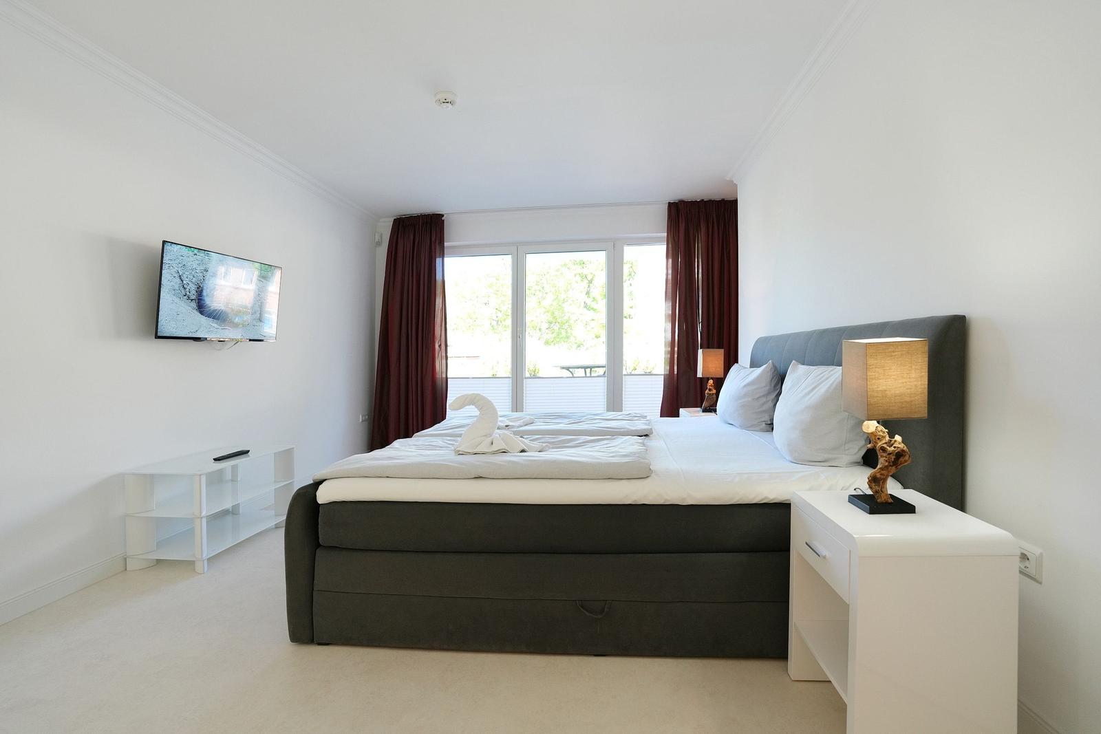 Schlafzimmer mit Bett, TV und Balkonansicht.