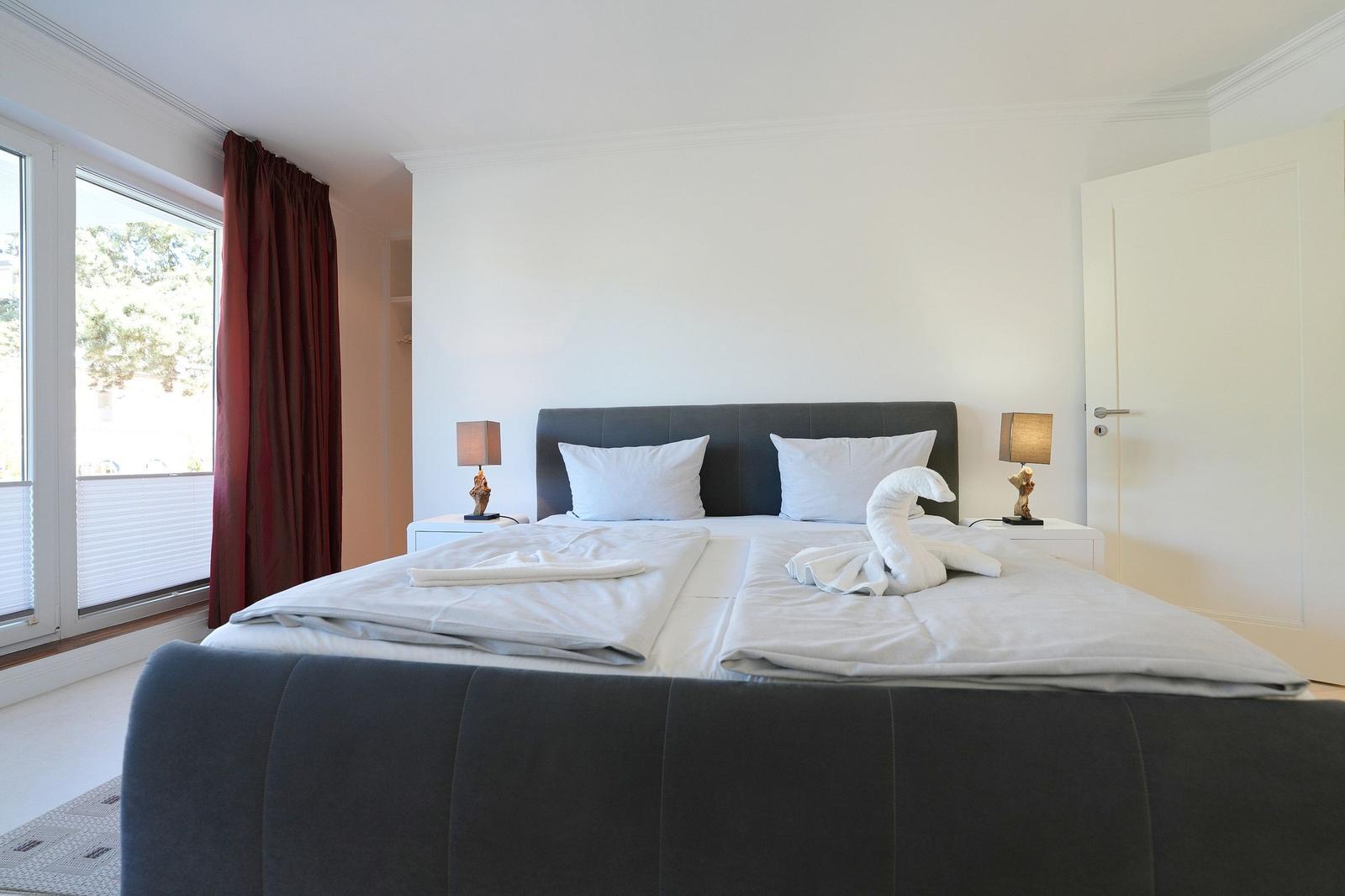 Schlafzimmer mit Doppelbett, weißen Kissen und einem weißen Handtuch in Form eines Schwans.