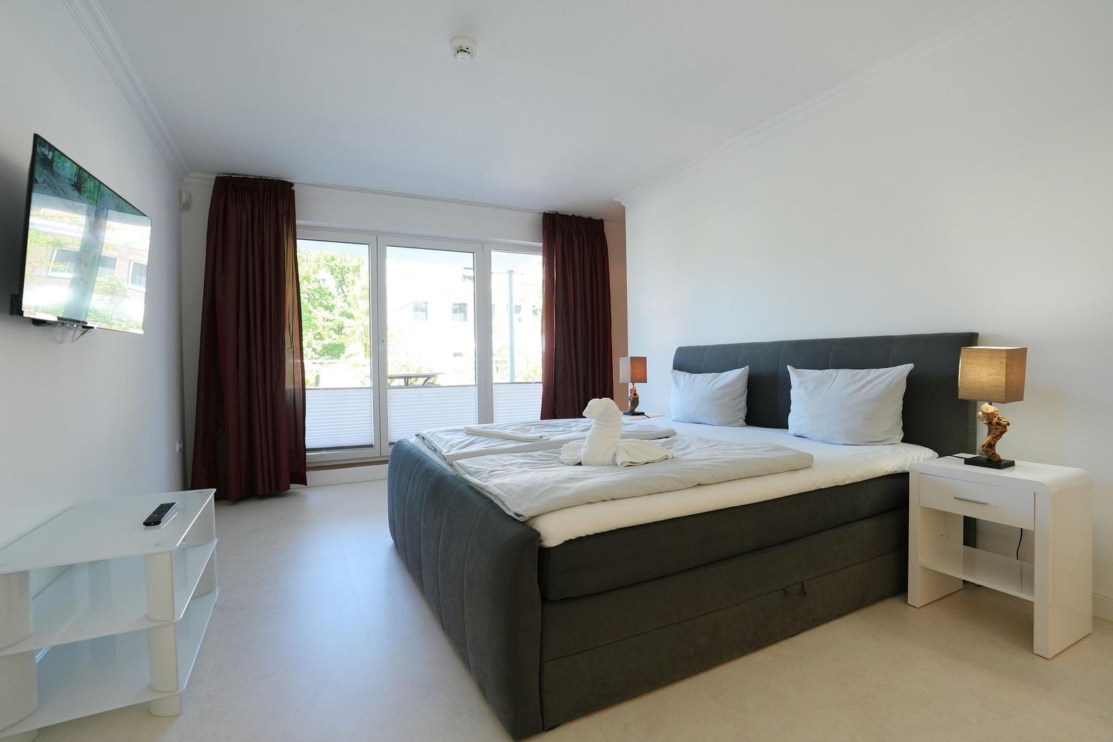 Schlafzimmer mit großem Bett, TV und Balkonansicht.
