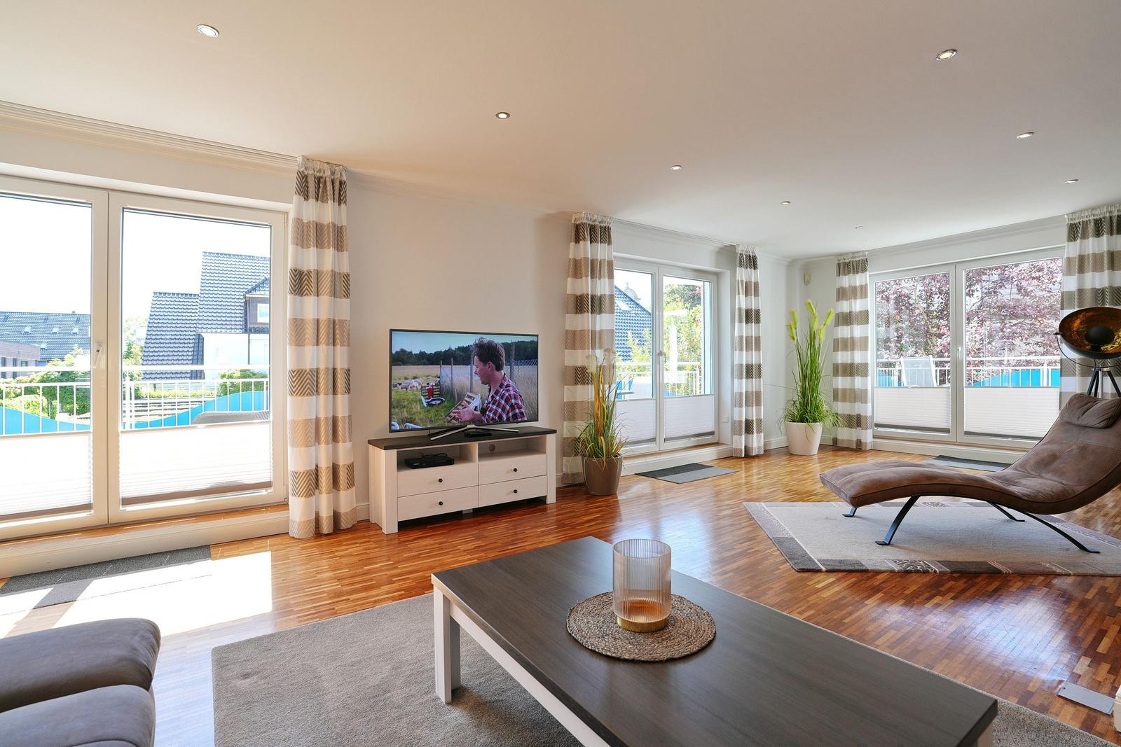 Wohnzimmer mit TV, Sitzgelegenheiten und Blick auf Balkon.