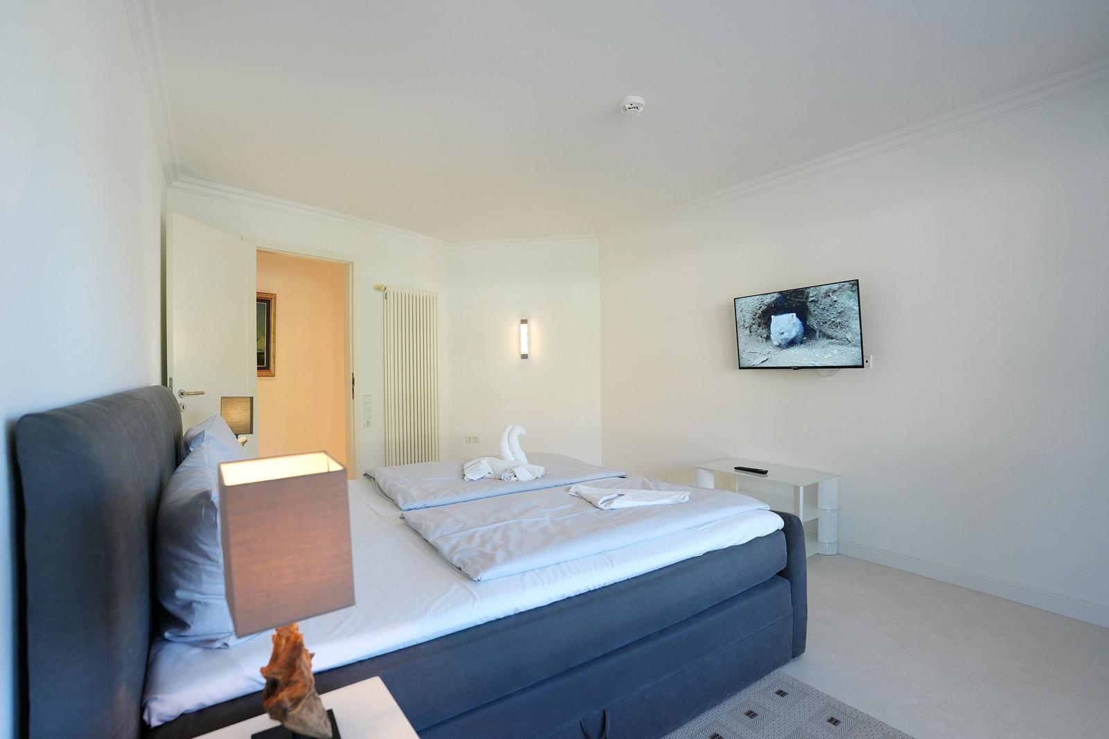 Schlafzimmer mit Doppelbett, Fernseher und Nachttisch.